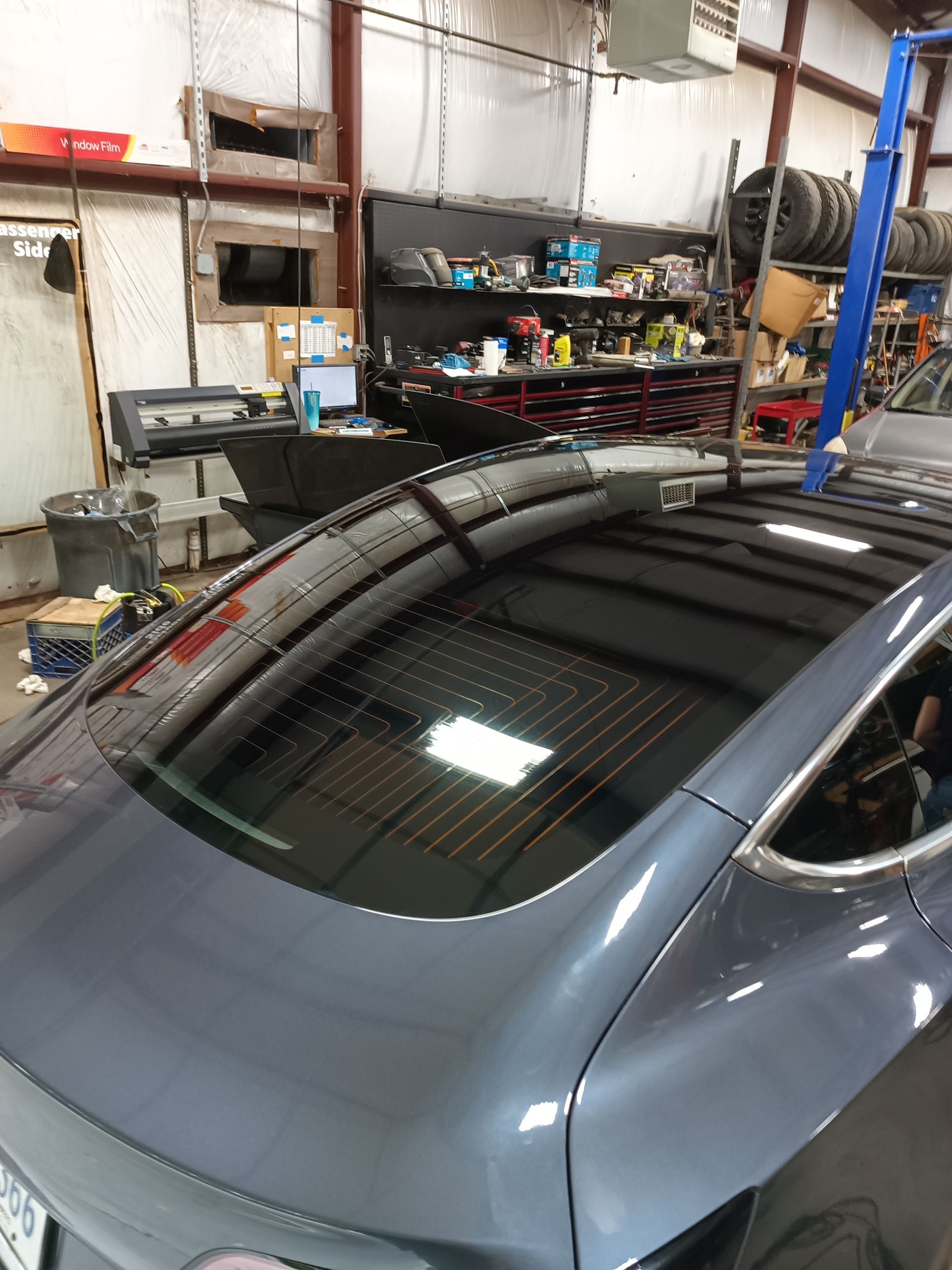 Gray car in a garage with tinted windows. The garage has tools and equipment.