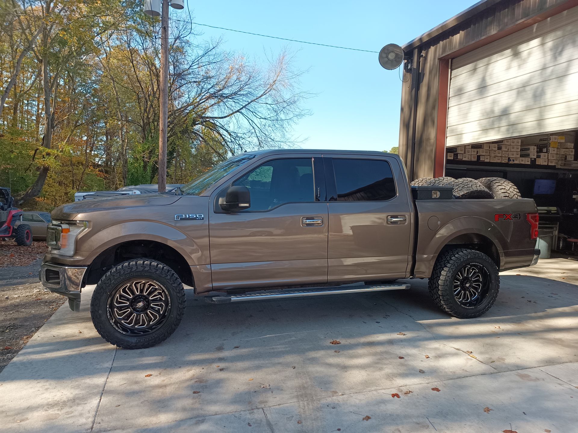 Brown Ford pickup truck parked in front of a garage, with large wheels and tinted windows.