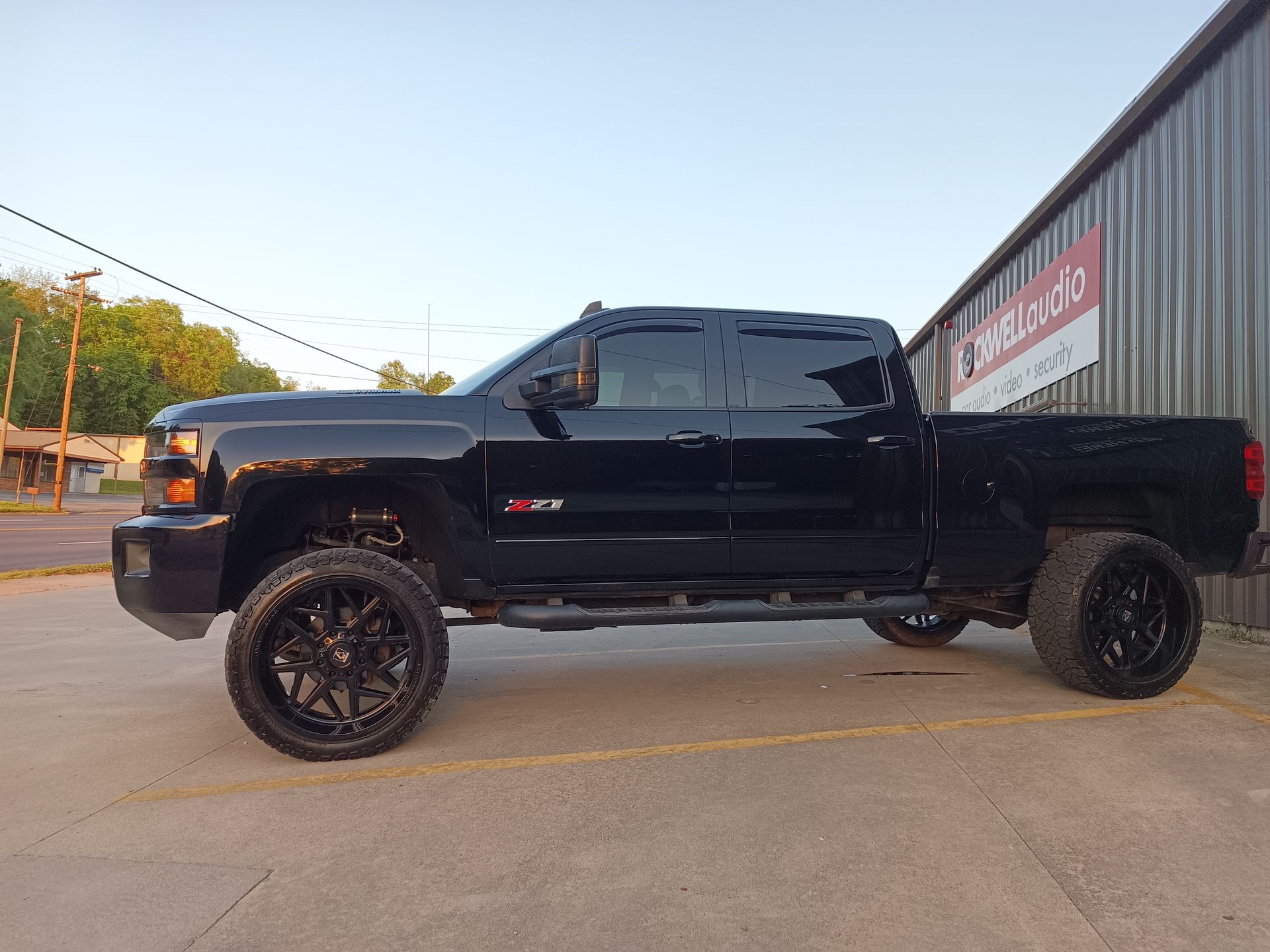 Black lifted Chevy Silverado truck parked outside a building with tinted windows and black rims.