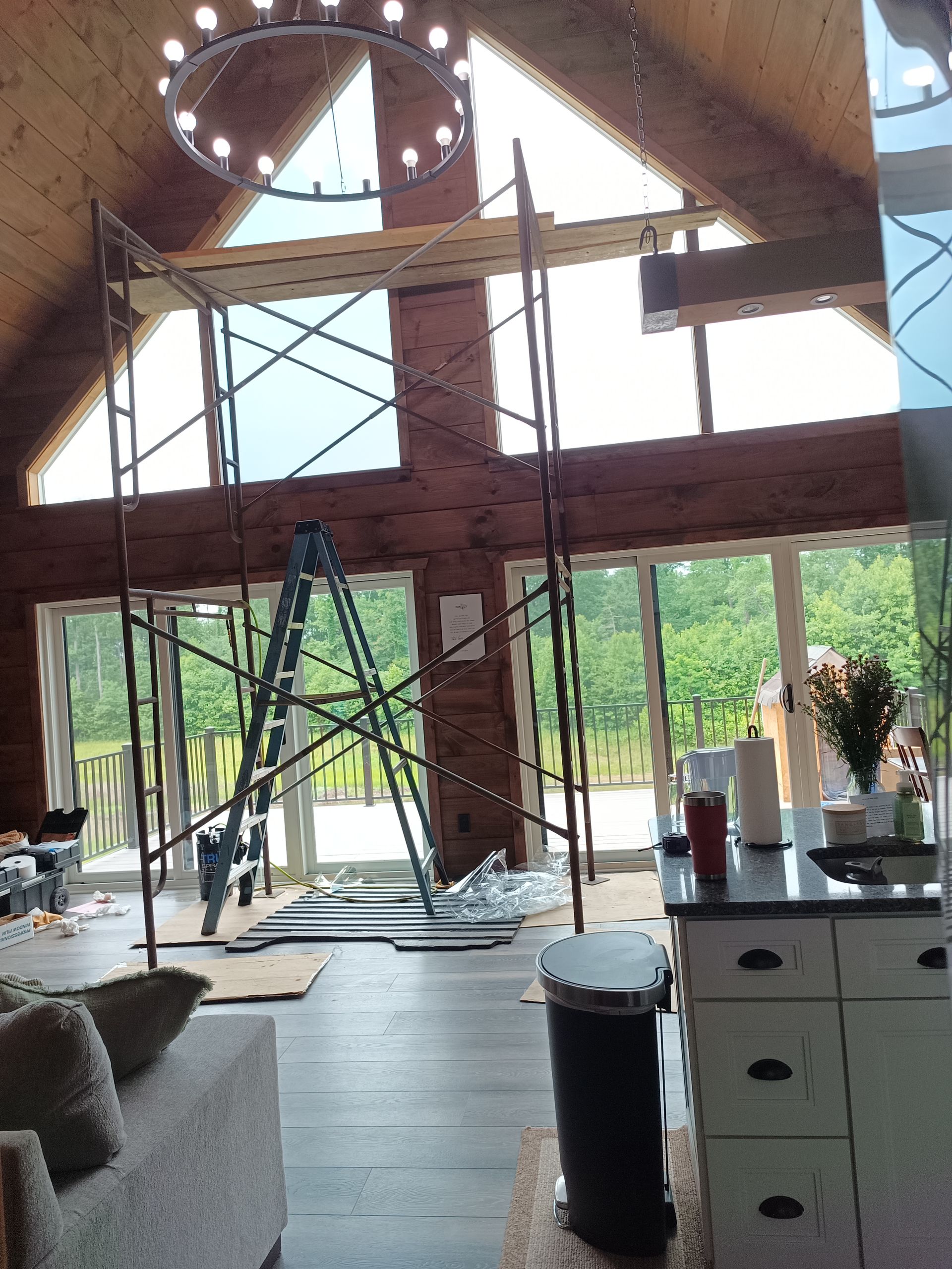 Interior view of a house with scaffolding set up near large windows, kitchen in the foreground.