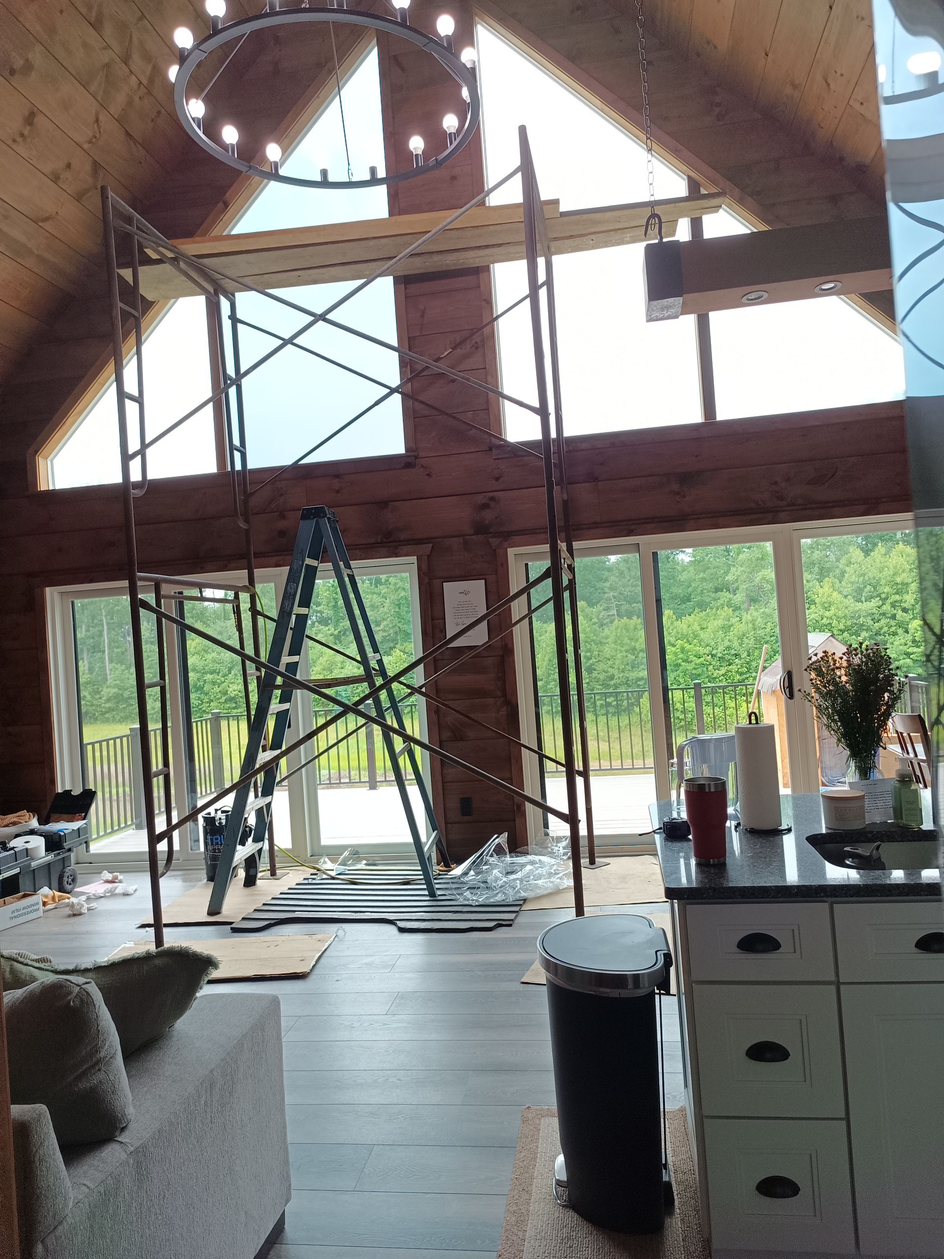 Interior: Scaffolding inside a home with tall windows. A kitchen island is in the foreground, with a sofa visible.