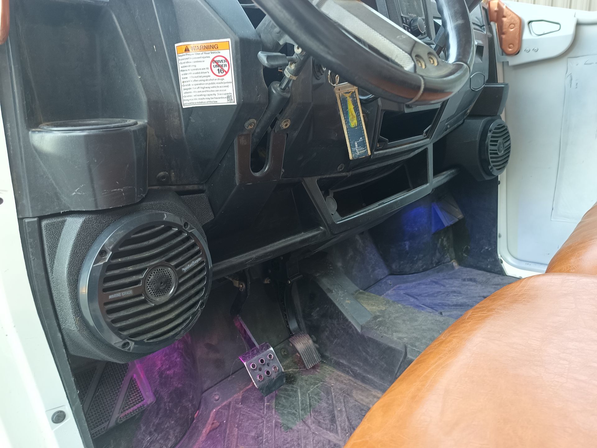 Interior of an off-road vehicle with speakers, steering wheel, and pedals; purple and green light.