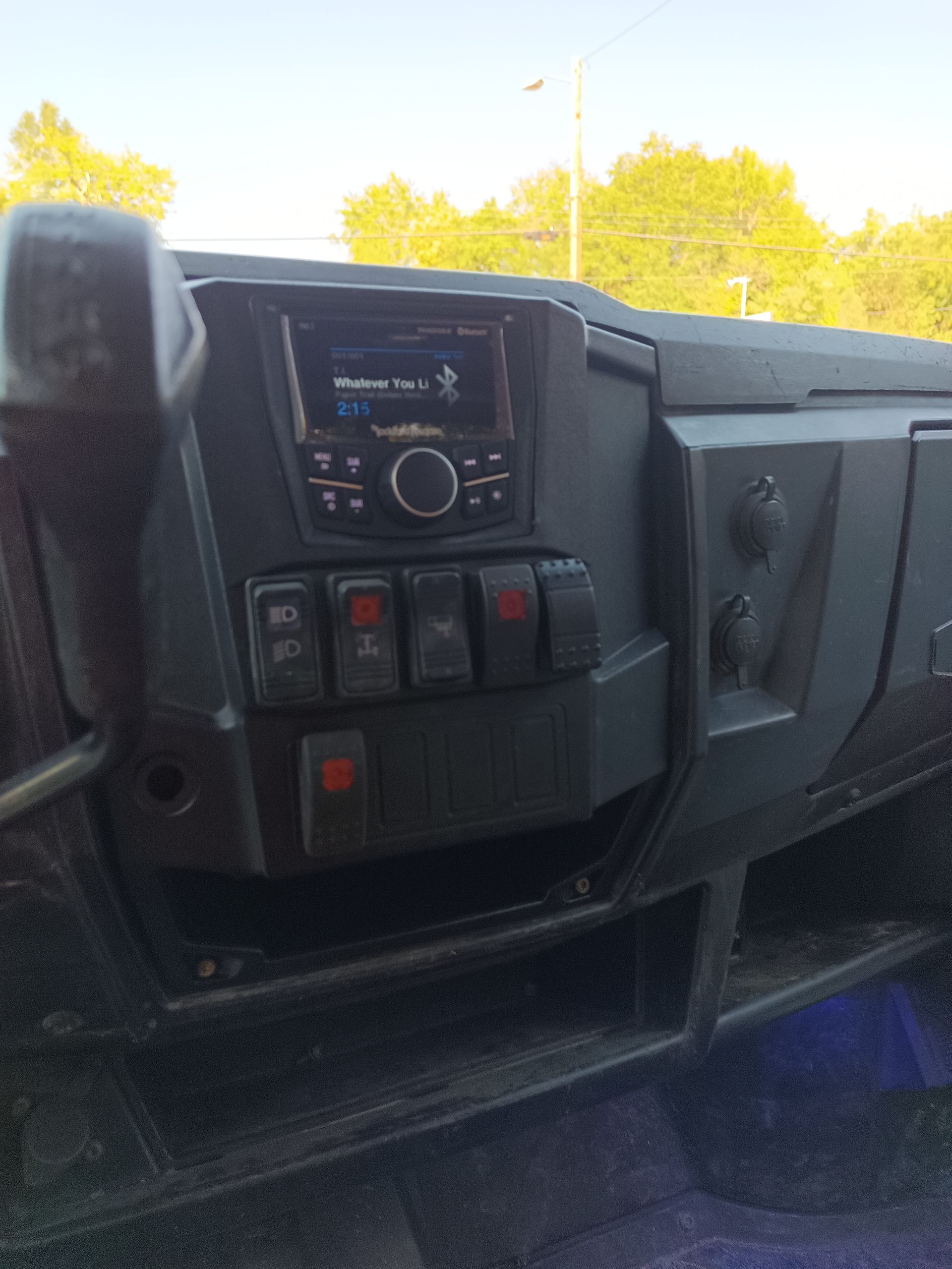 Dashboard of a black utility vehicle with a radio, switches, and a power outlet.