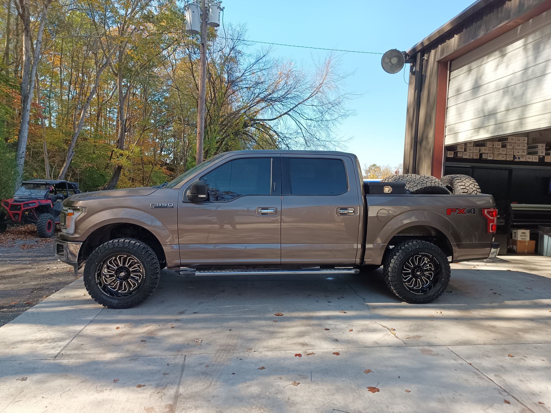 Tan Ford F-150 truck with tinted windows and black wheels parked outdoors, near a building and trees.