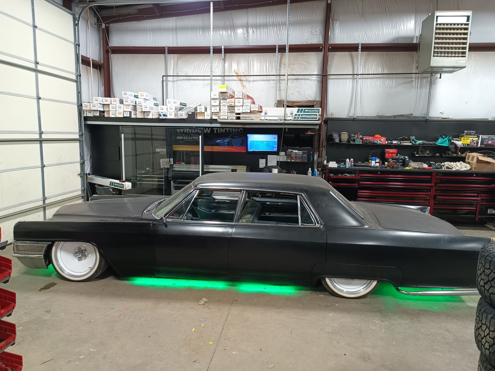 Black classic car in a garage with green underglow; white rims.