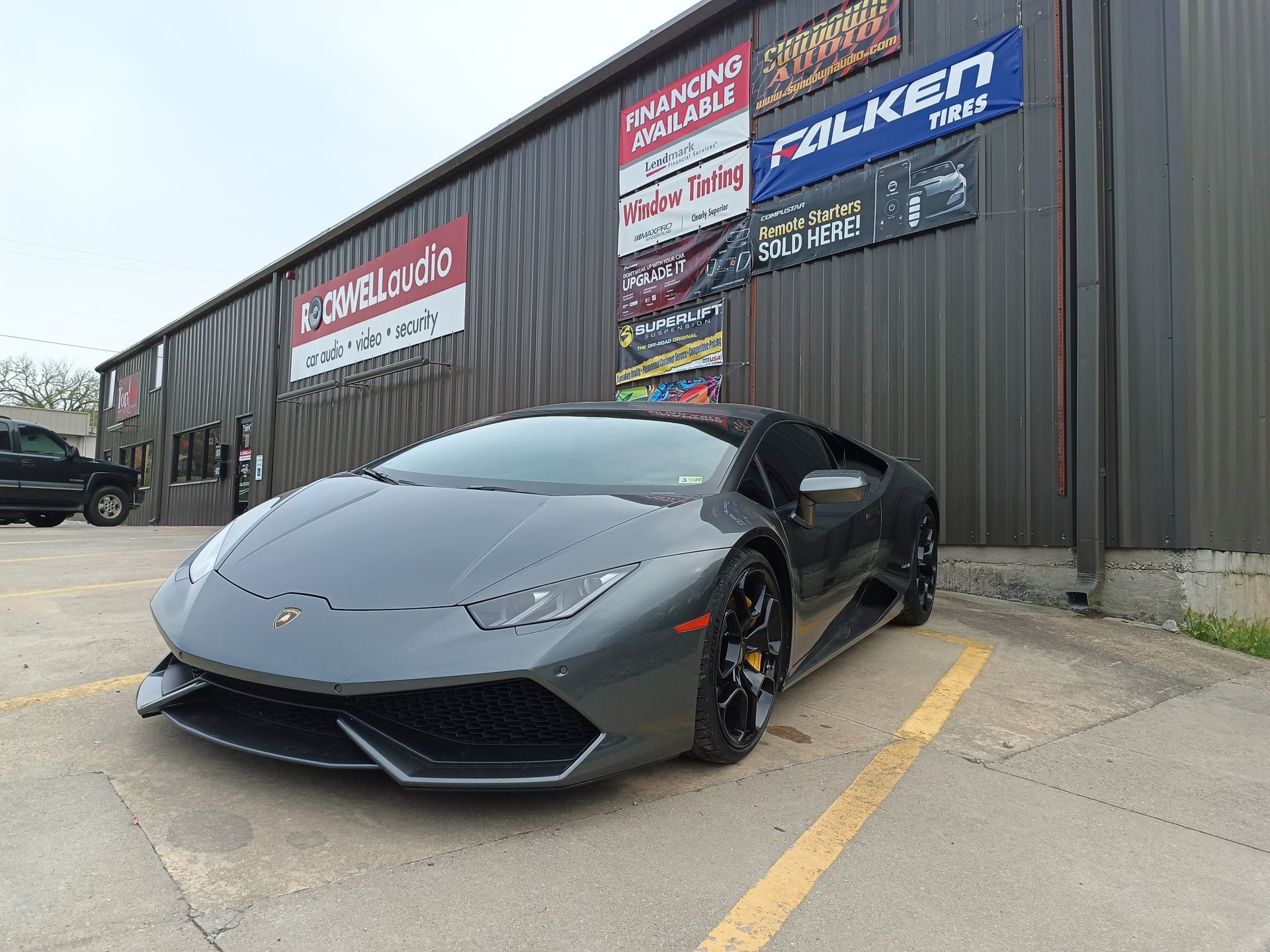 Gray Lamborghini sports car parked outside a building with tire company signs.