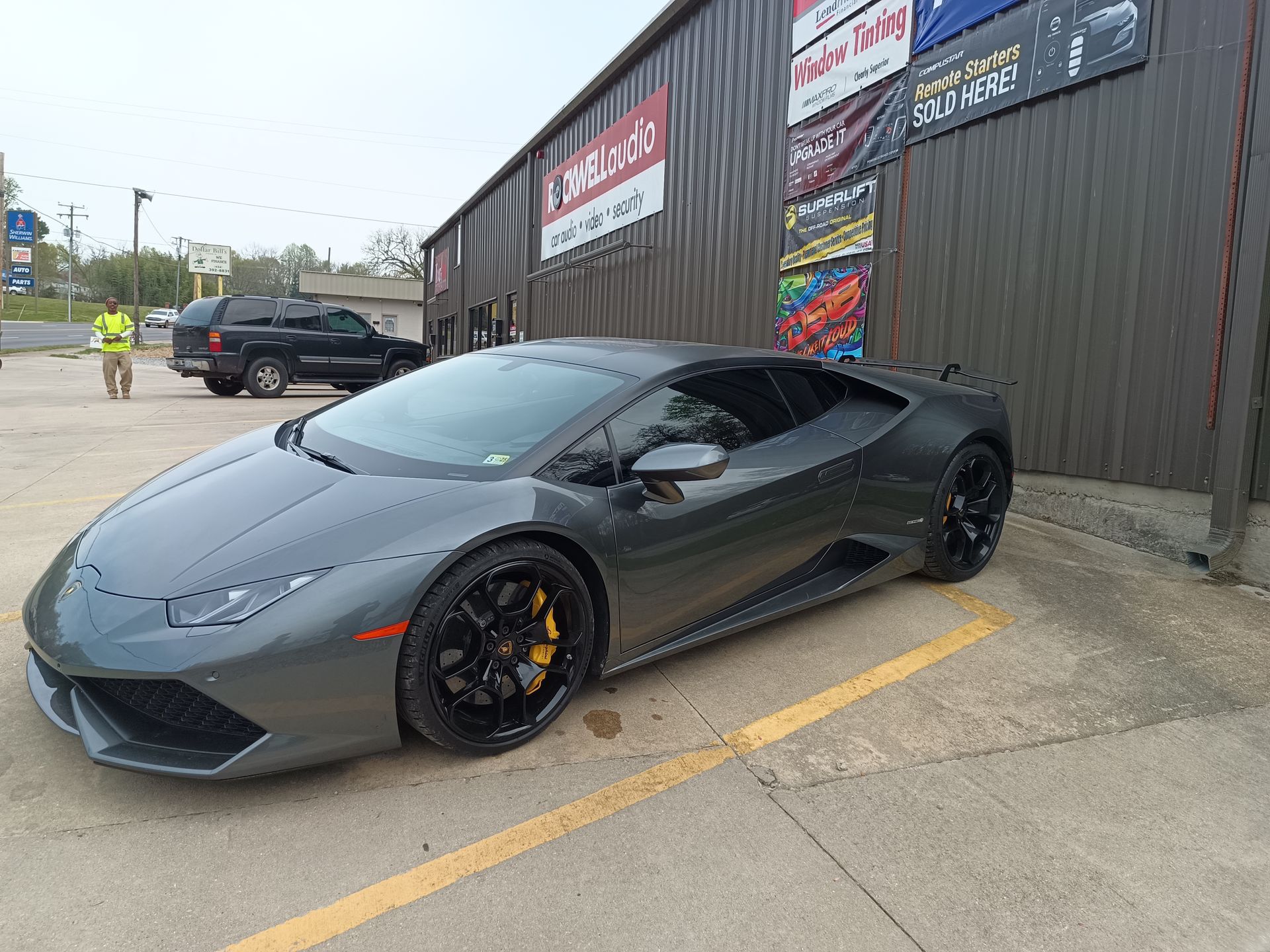 Gray Lamborghini parked outside a business with a person standing nearby.
