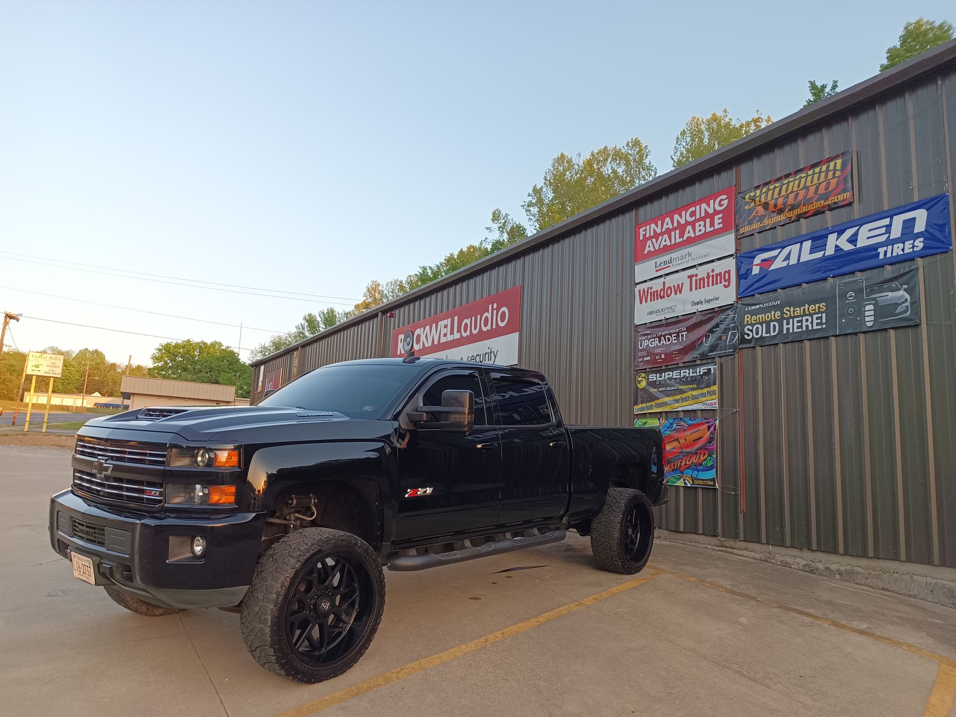 Black pickup truck parked outside a business with promotional signs.