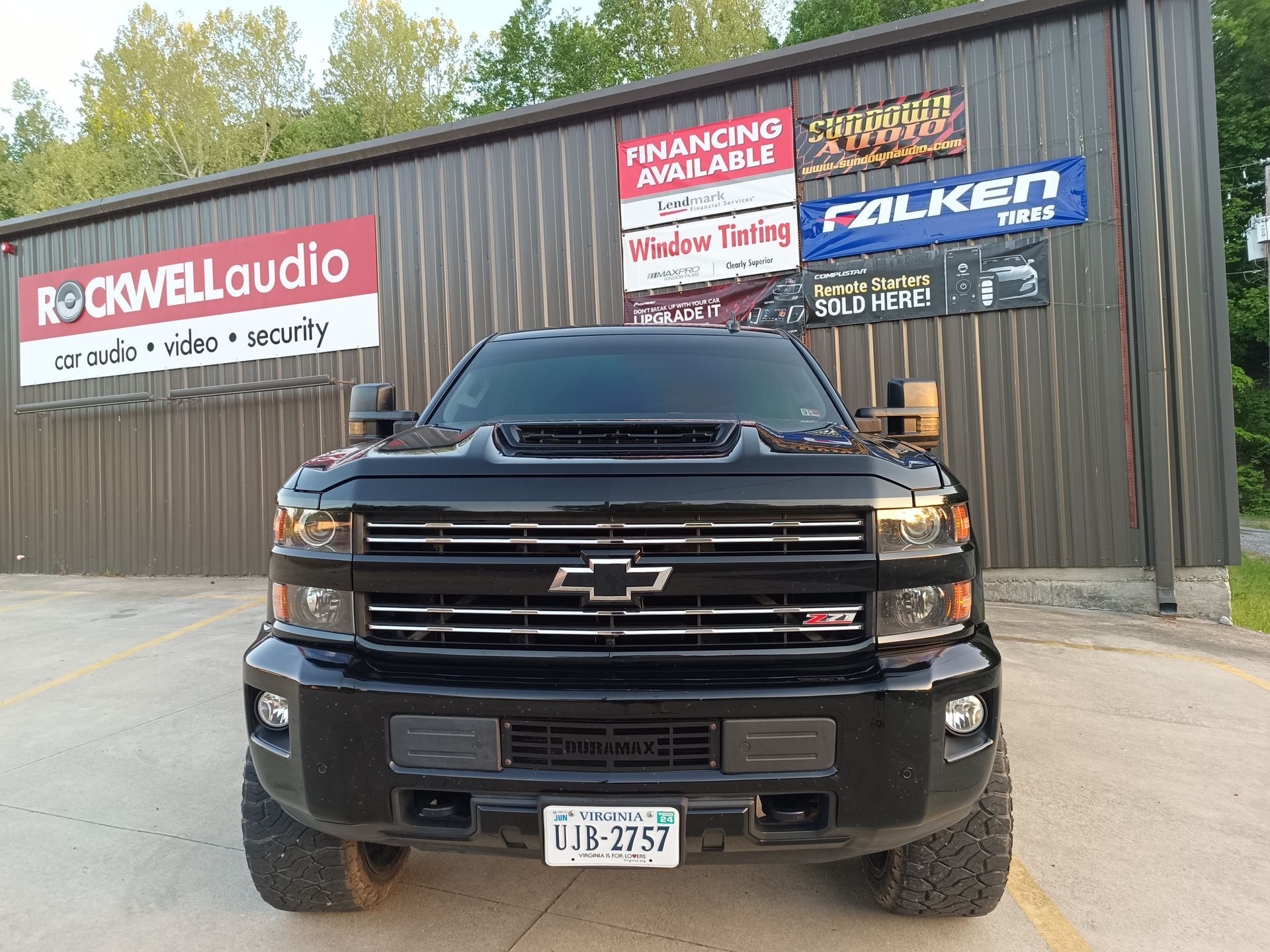 Black Chevrolet truck parked in front of a building with signs for audio, tires, and financing.