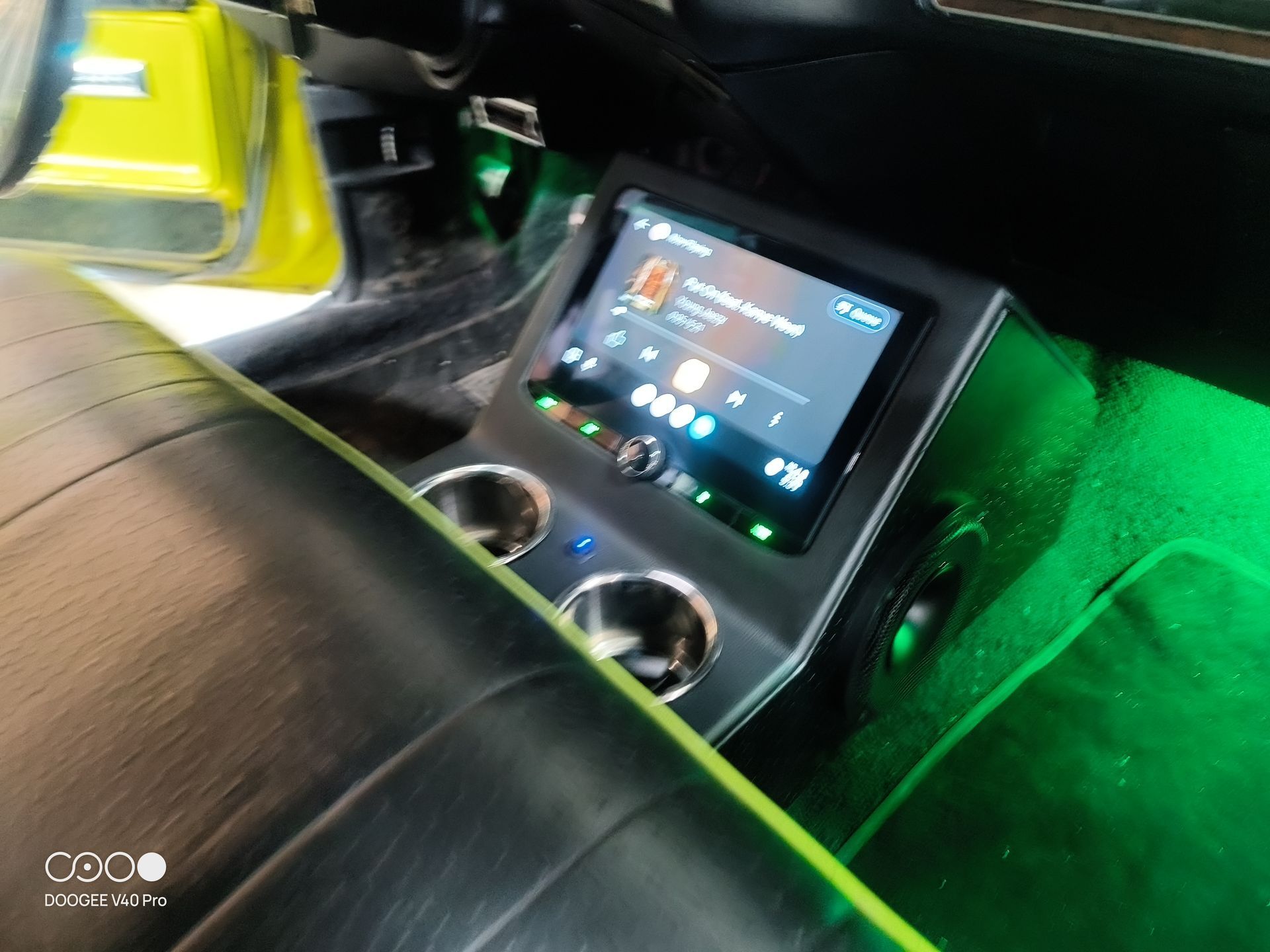 Custom car console with infotainment screen, cupholders, and green underglow lighting.