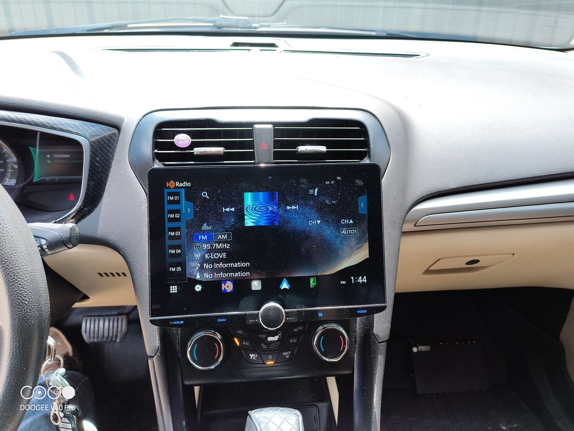 Dashboard of a car with a large touchscreen displaying a music interface, beige and black interior.