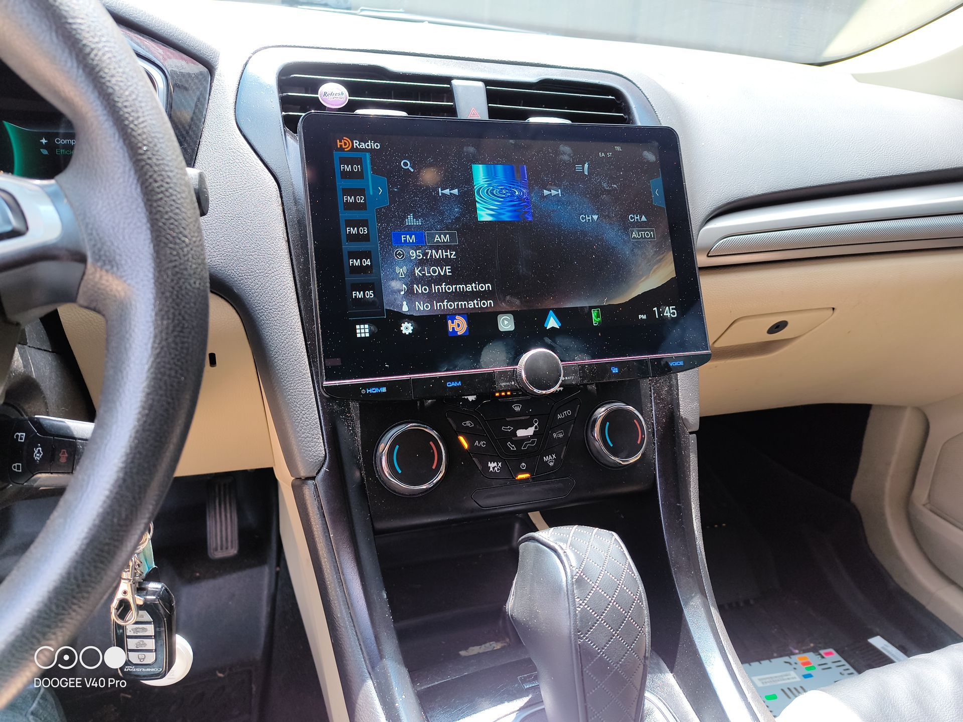 Car interior with large touchscreen display, climate controls, gear shift, steering wheel, and car keys.
