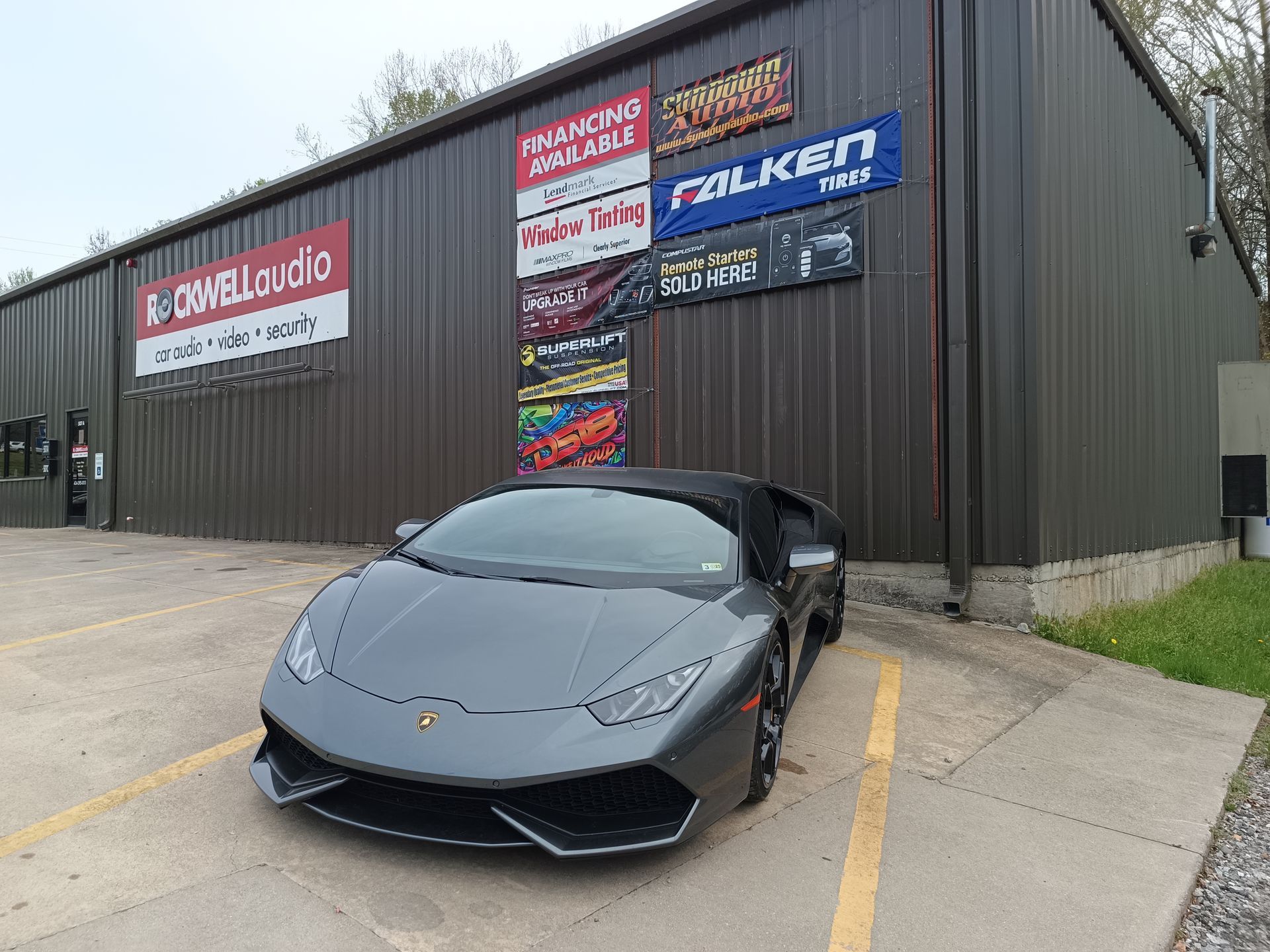Gray Lamborghini convertible parked in front of a building with signs.