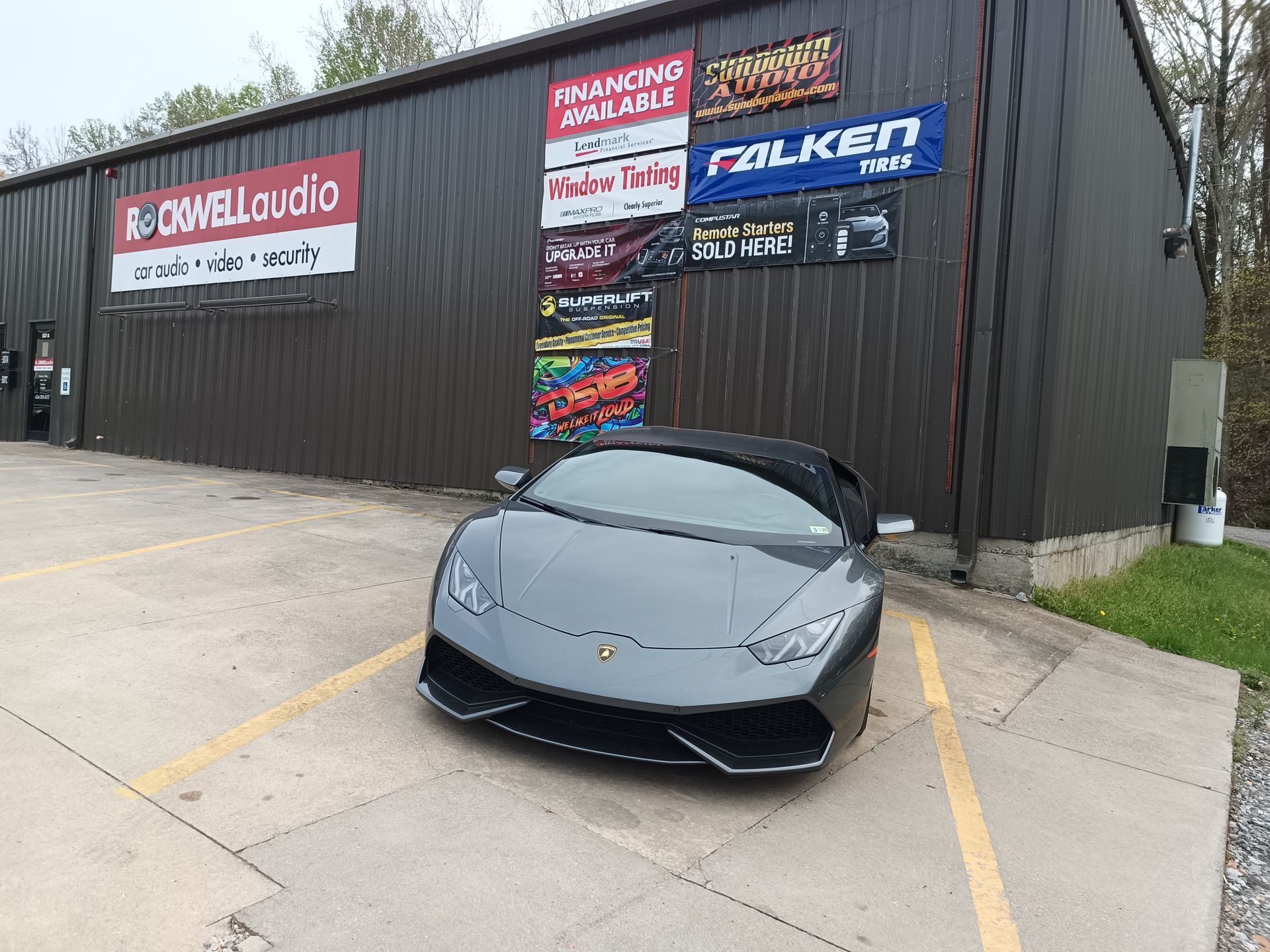 Gray Lamborghini parked in front of a building with car audio and tire signage.