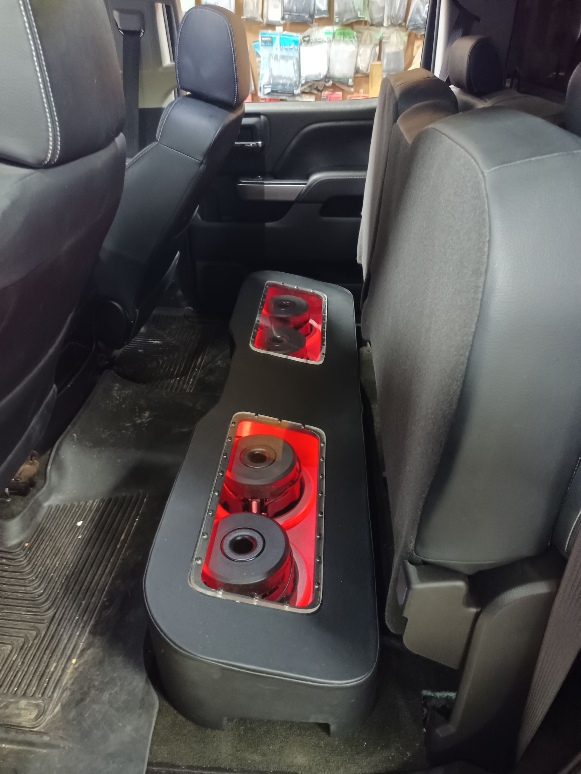 Custom car audio subwoofer enclosure in the rear seat area of a vehicle, black with red accents.