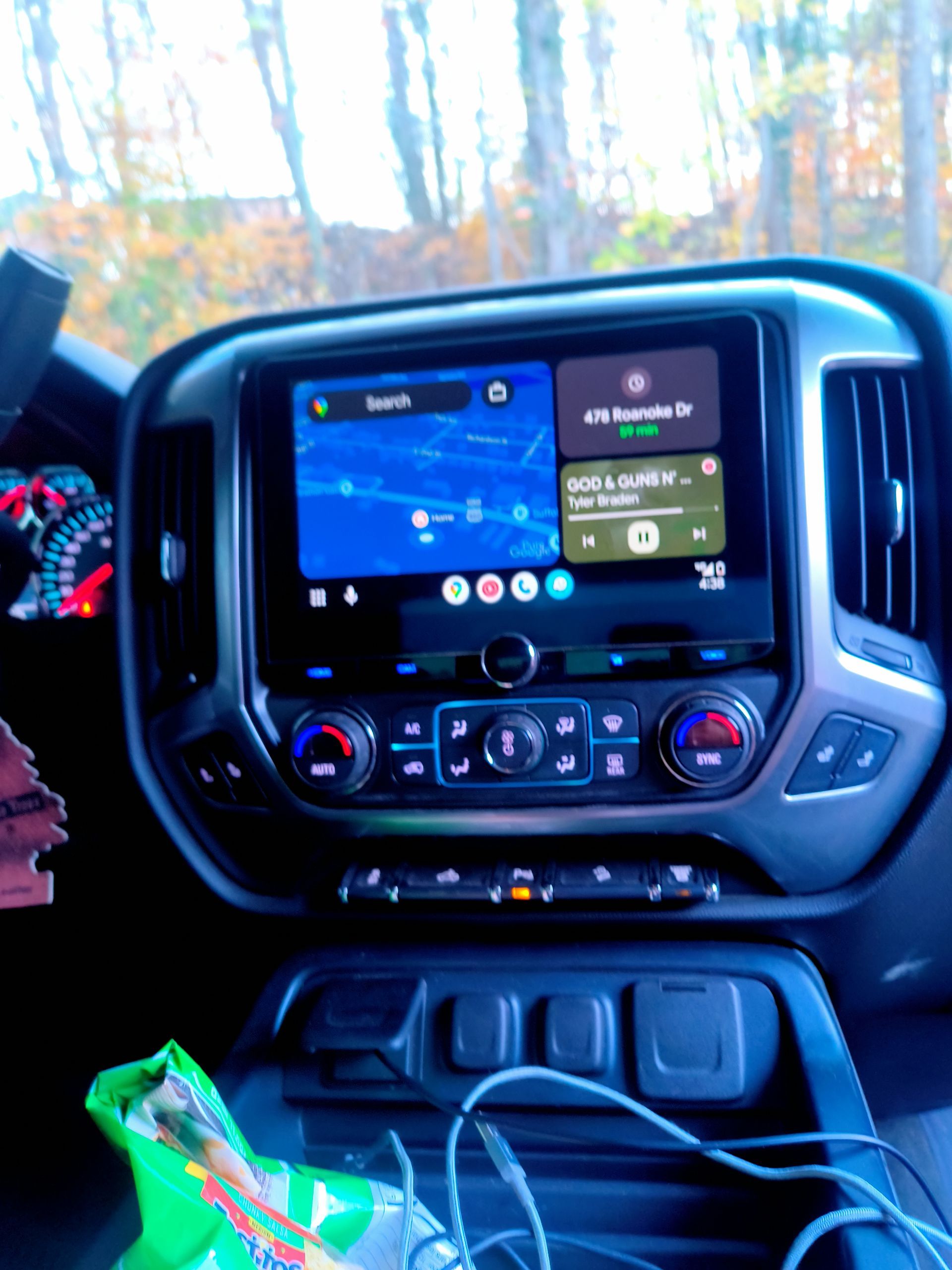 Car interior with GPS navigation screen, music controls, and air vents.  Forest visible in the background.