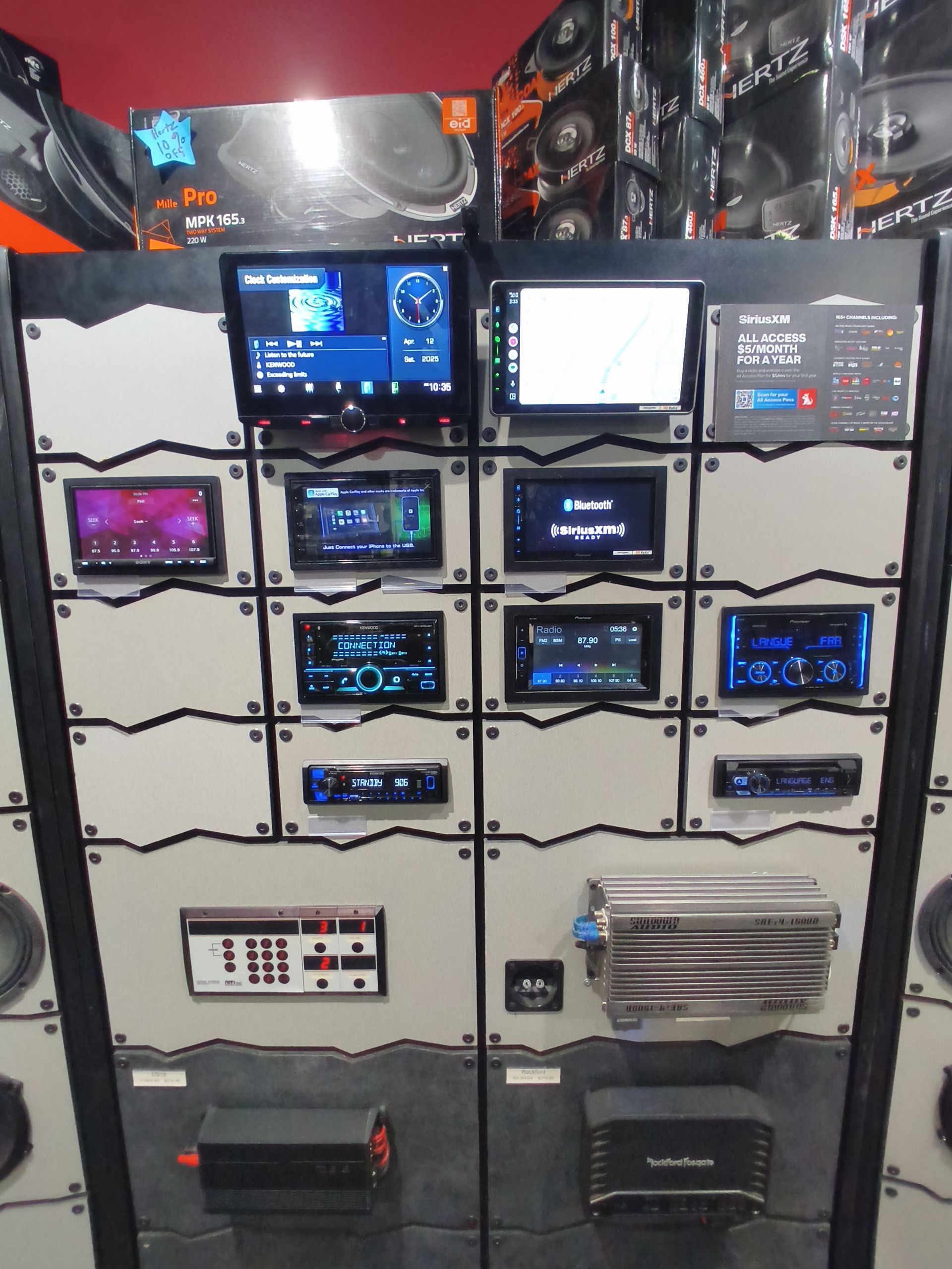 Car audio equipment display with various head units, amplifiers, and speakers.
