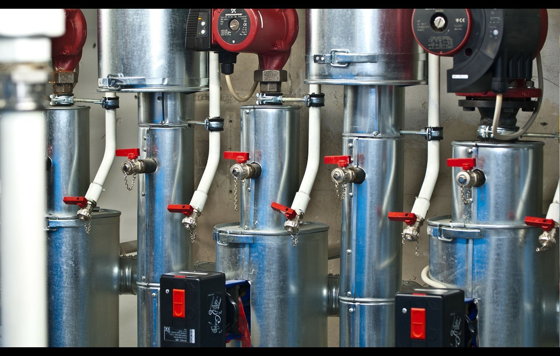 Metallic pipes and valves with red handles in a mechanical room, featuring circulation pumps.