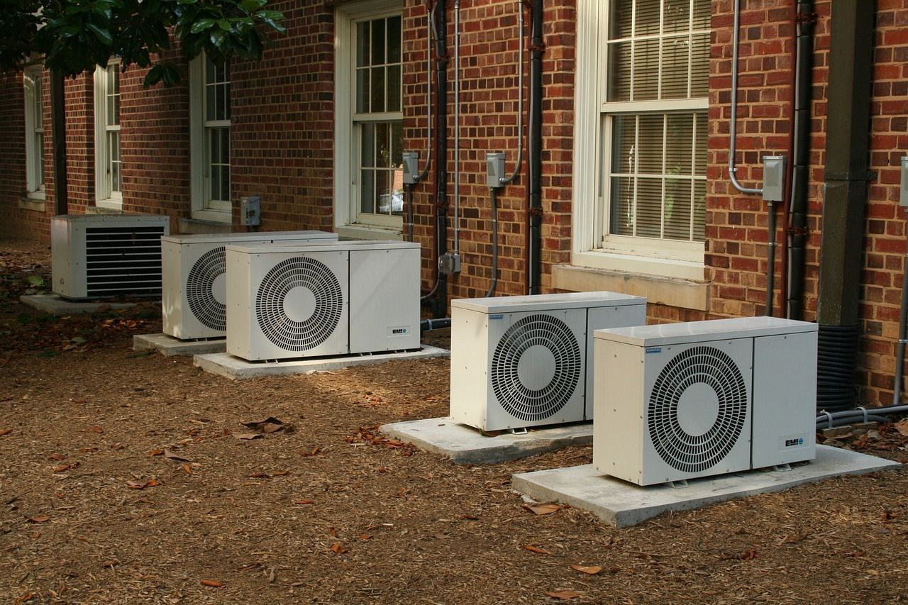 Exterior air conditioning units sit on concrete pads outside a brick building.