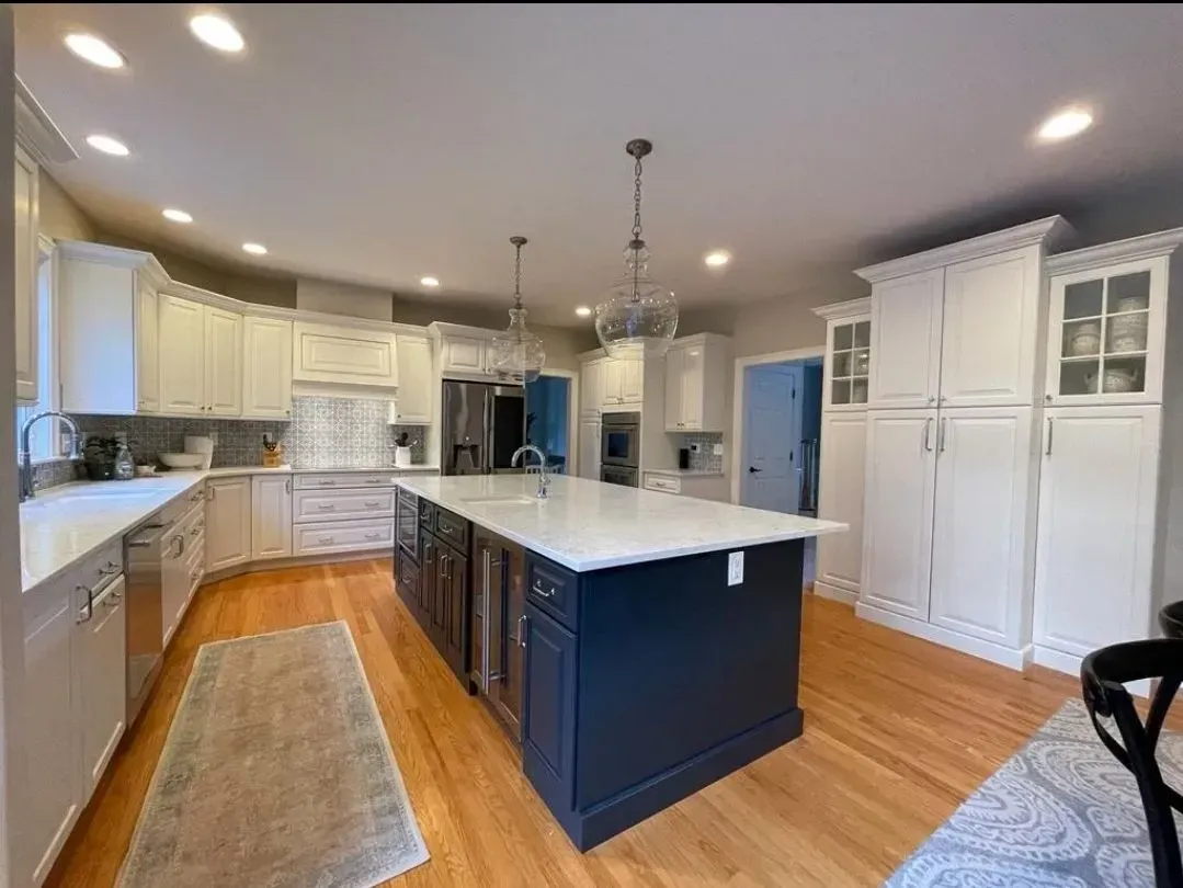 Spacious kitchen with dark blue island and white cabinets on wood floors.