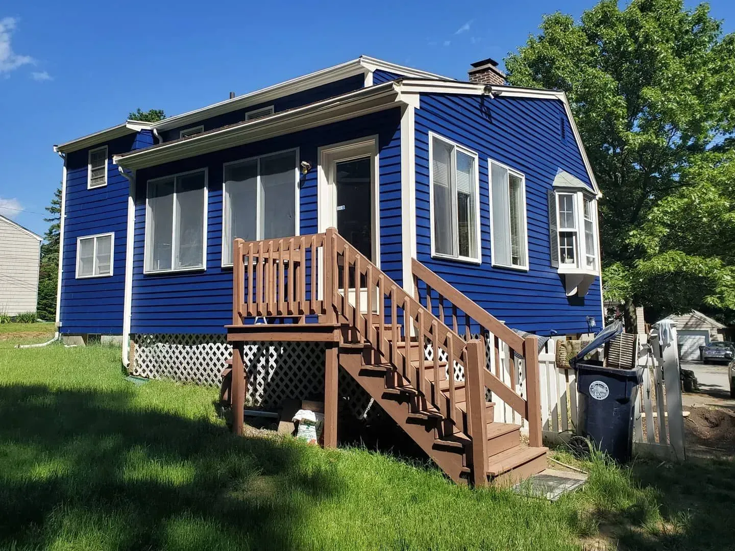 Blue house with brown stairs and white trim in a yard on a sunny day.