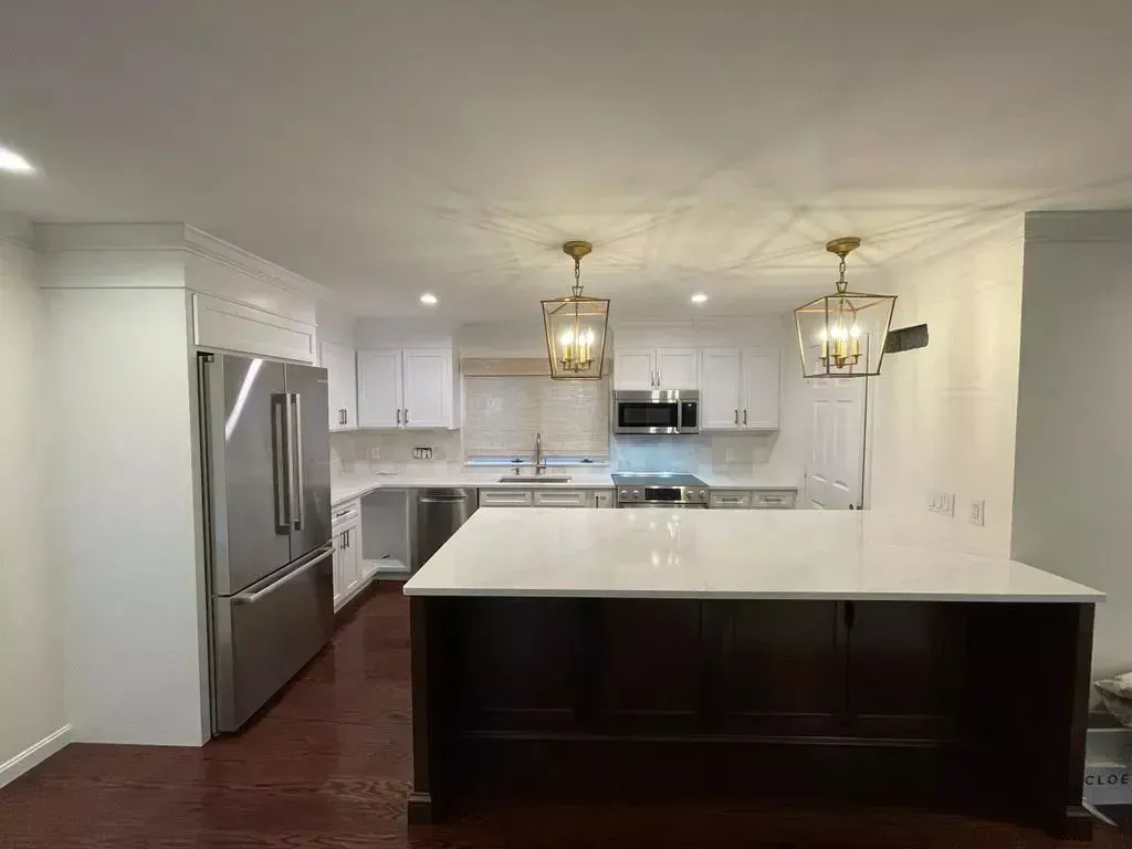 Modern kitchen with white cabinets, stainless steel appliances, dark wood island, and gold light fixtures.
