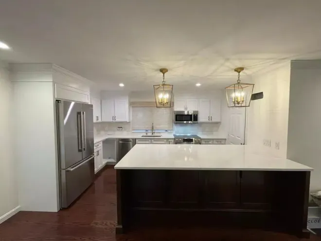 Modern kitchen with white cabinets, stainless steel appliances, dark wood island, and gold light fixtures.