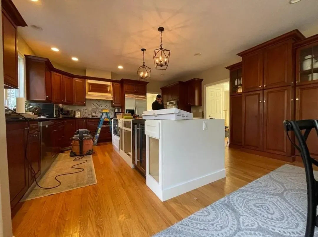 A kitchen with brown cabinets, a white island, and hardwood floors. Construction in progress.