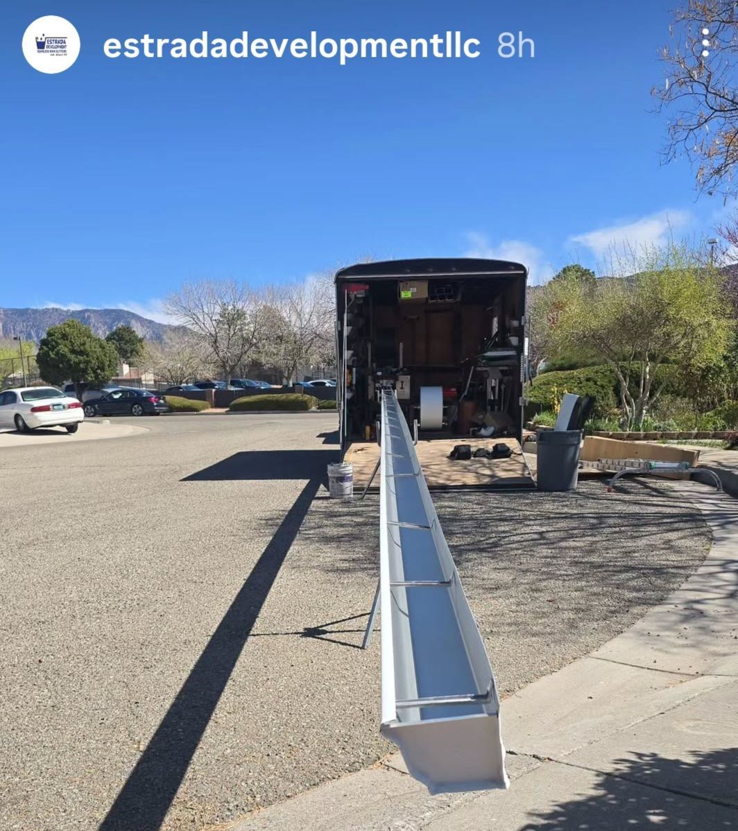 Long metal gutter/chute extending from a truck parked in a lot on a sunny day