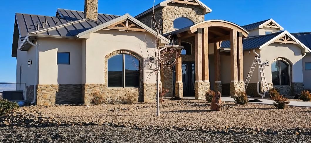 A large beige house with stone accents, arched windows, and a blue sky.