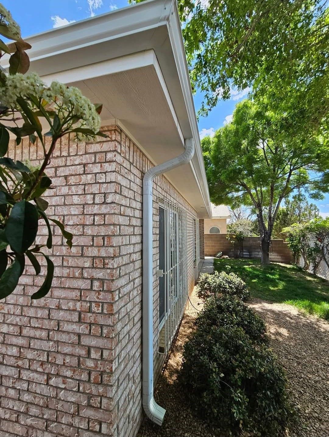 Brick house exterior with white trim, gutters, and green foliage against a blue sky.