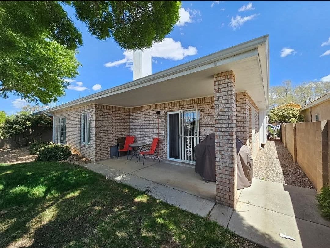 Brick house with covered patio, red chairs, and sliding glass door. Overcast sky.