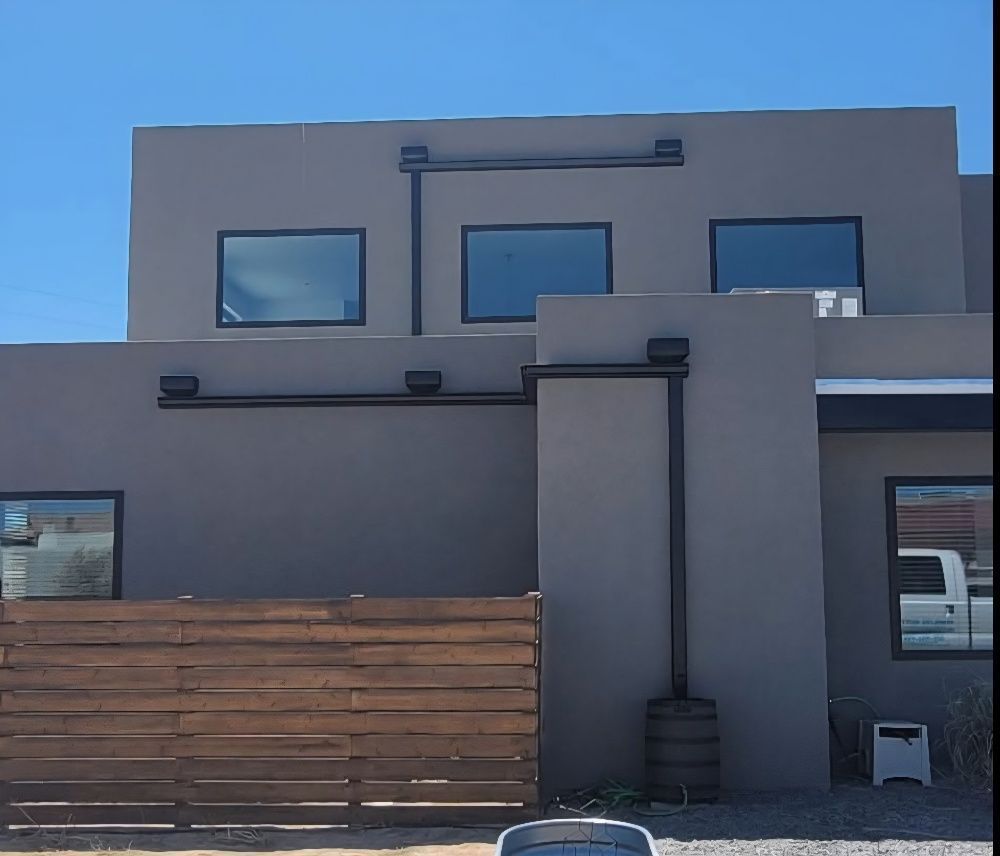 Gray building with black accents windows and wooden fence in front.