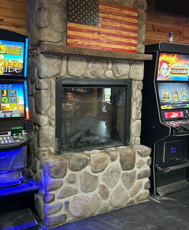 A fireplace with a brick surround, wooden mantel supported by three corbels, black mesh screen, and iron tool set.