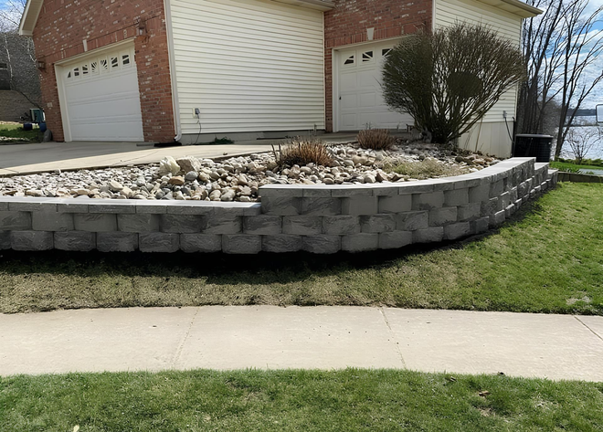 A curved retaining wall made of textured, alternating gray and reddish-brown stone blocks next to a paved patio.