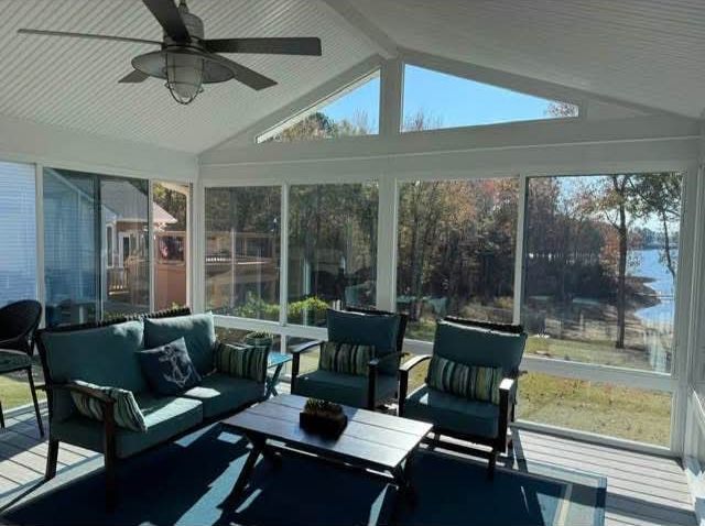A screened in porch with a couch, chairs, table and ceiling fan.
