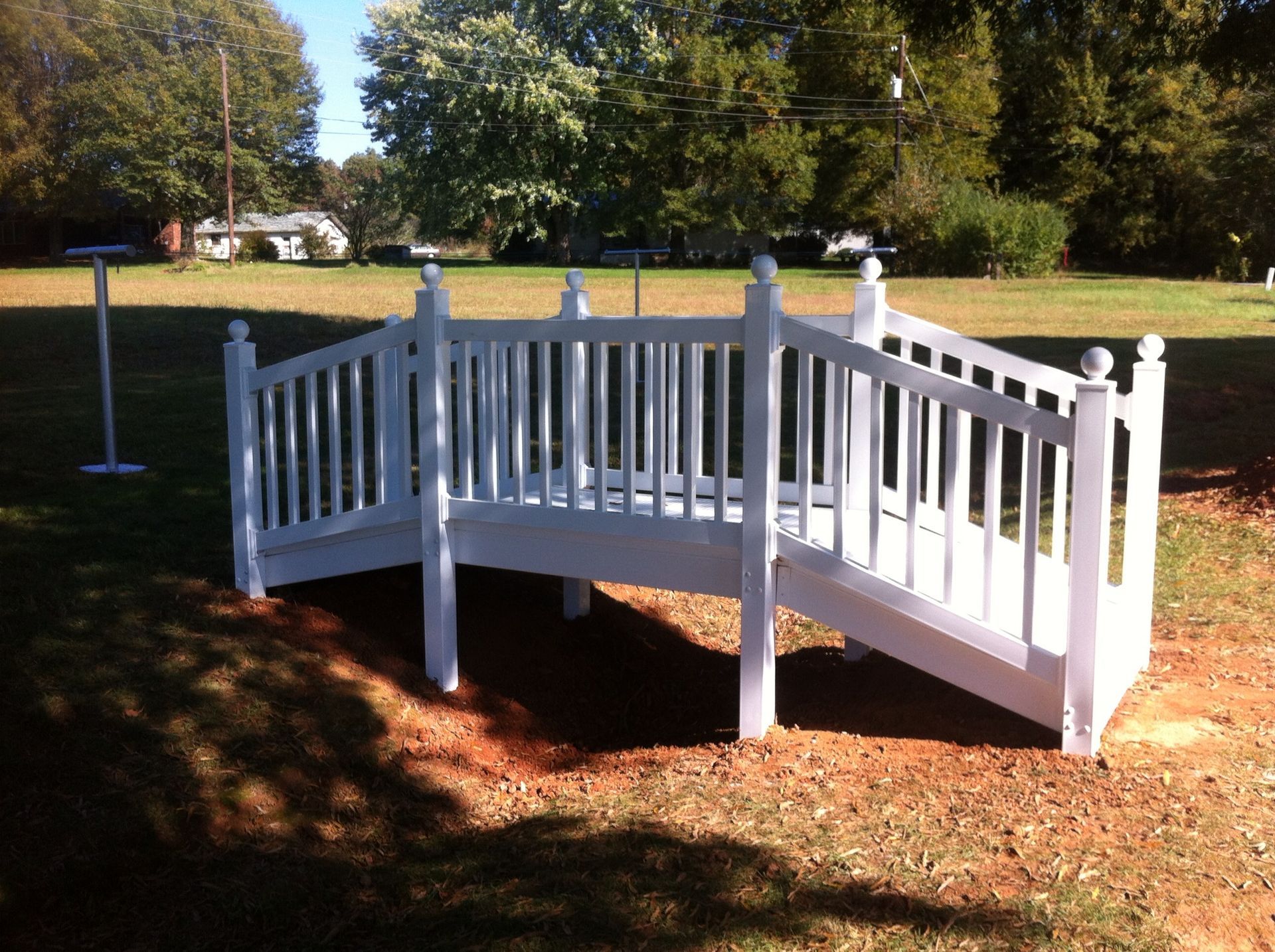 A white wooden bridge is in the middle of a grassy field