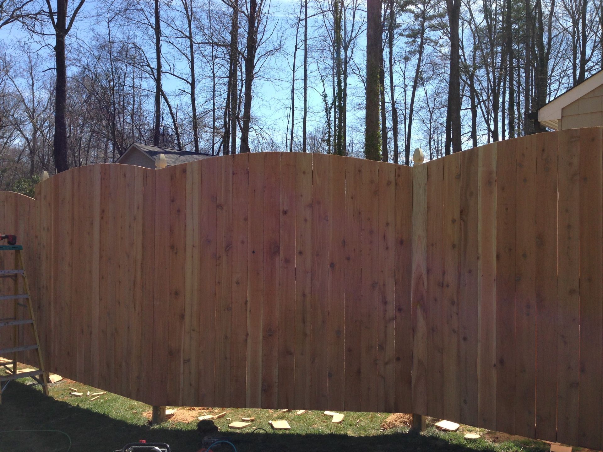 A wooden fence is being built in a backyard with trees in the background.