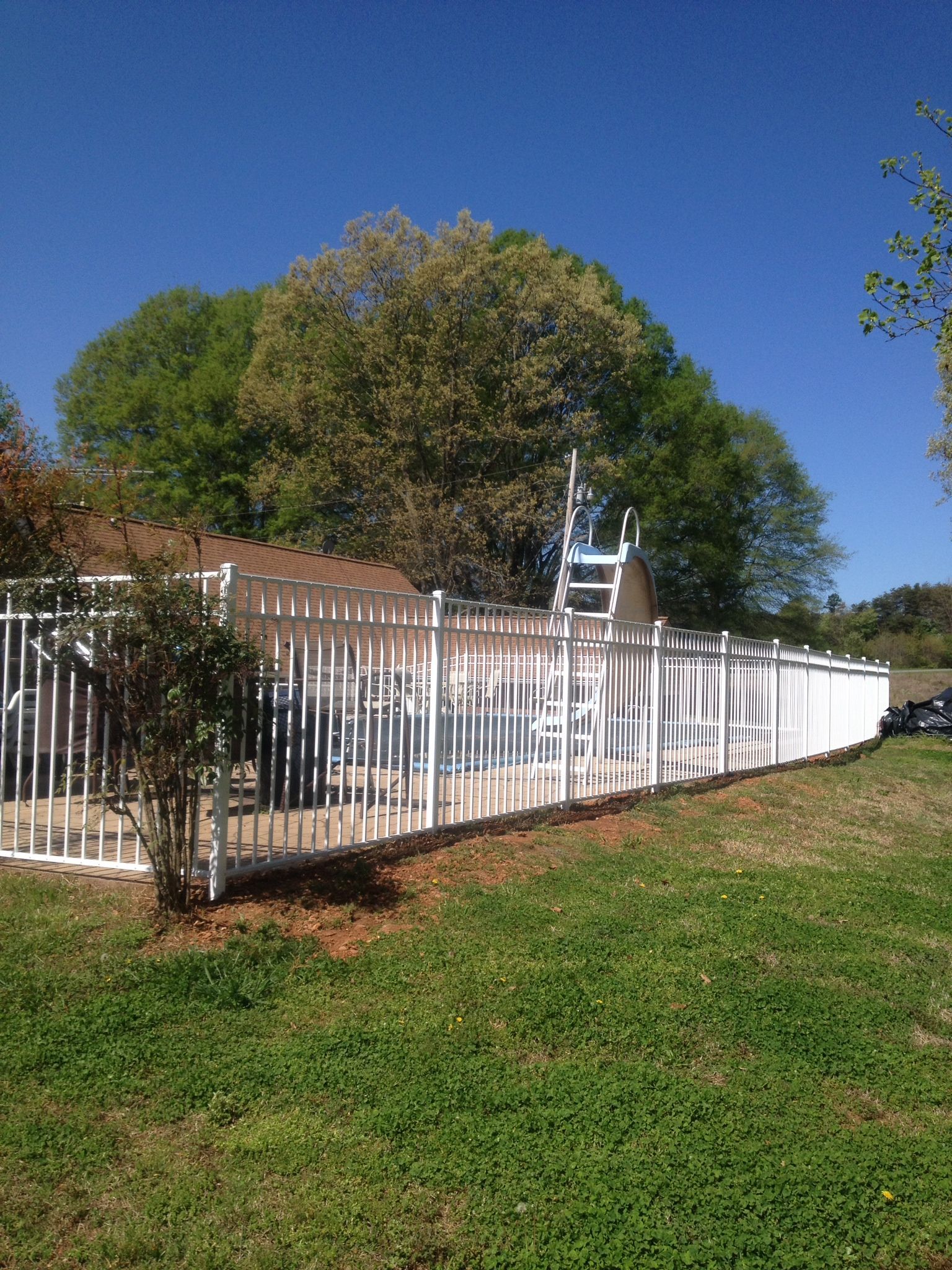 A white fence surrounds a swimming pool in a yard.