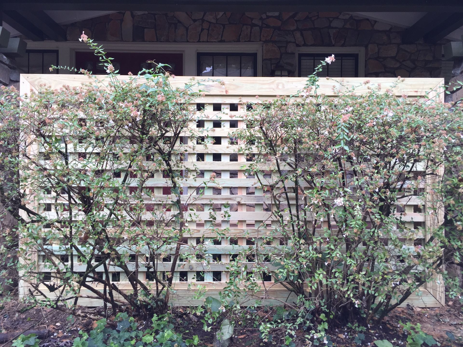 A wooden fence is surrounded by bushes in front of a house