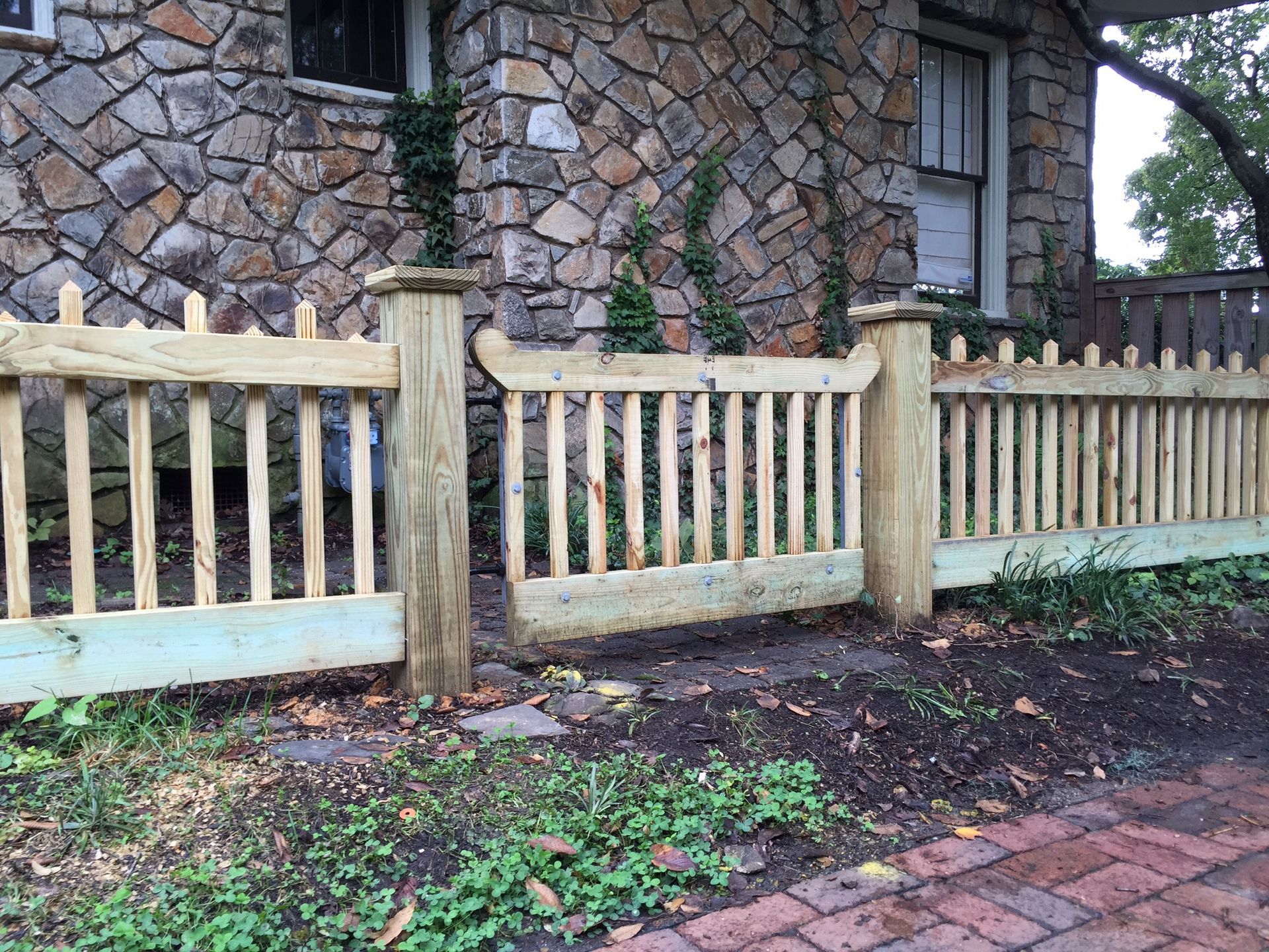 A wooden fence is in front of a stone house.