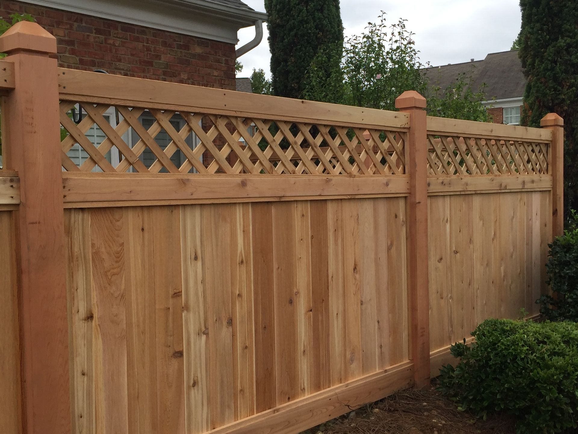 A wooden fence with a lattice design is in front of a brick house.