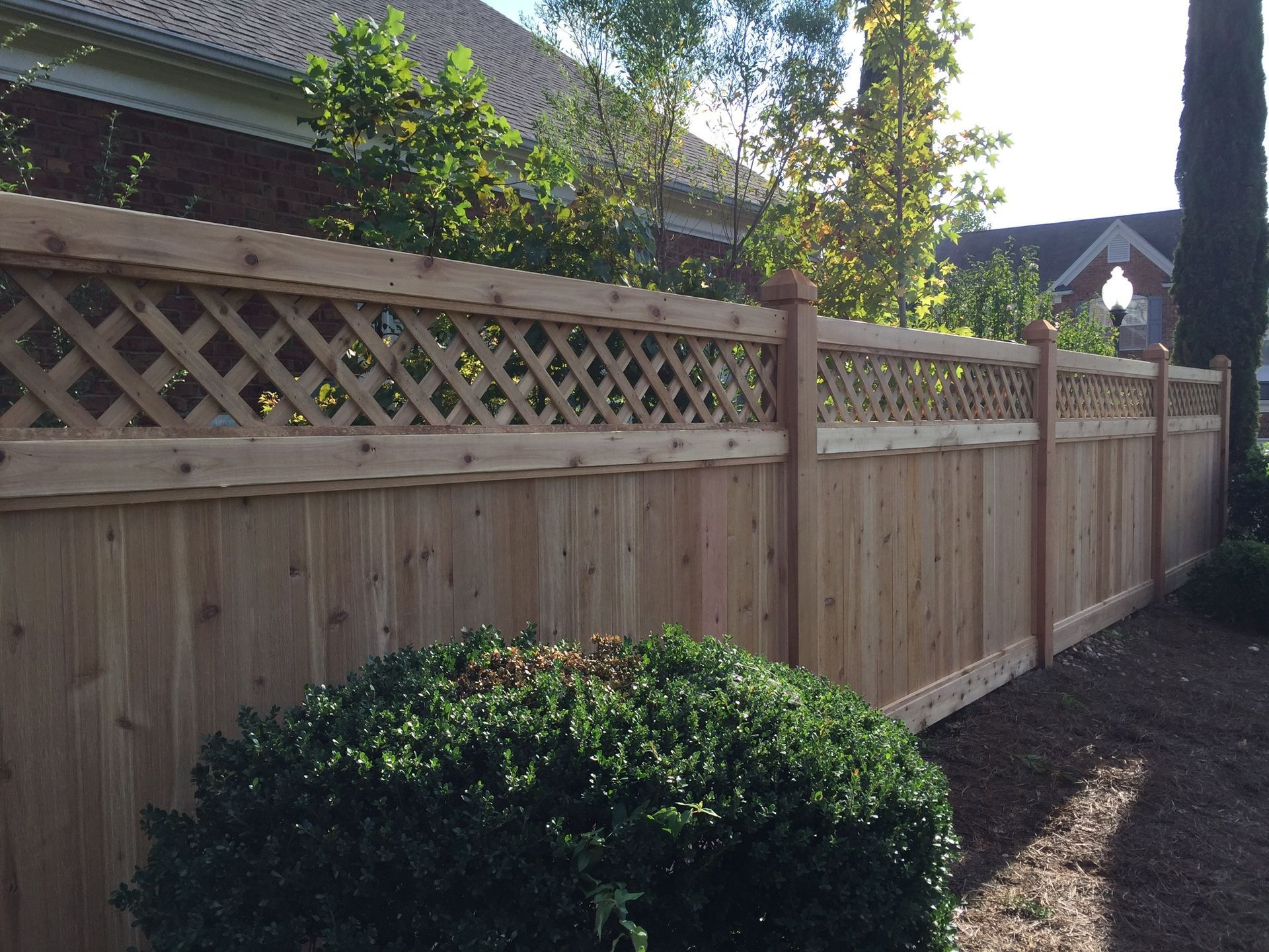 A wooden fence with a lattice design is surrounded by bushes and trees.