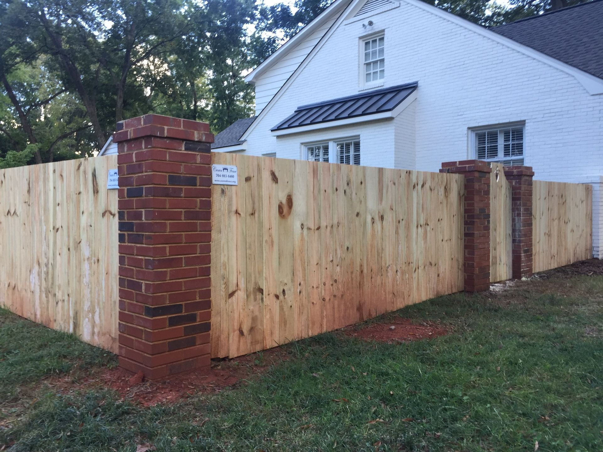 A wooden fence with brick posts in front of a white house.