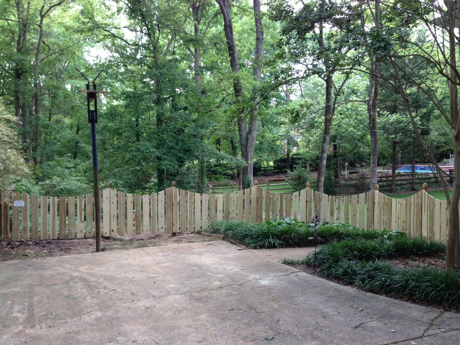 A wooden fence surrounds a driveway in the middle of a forest.