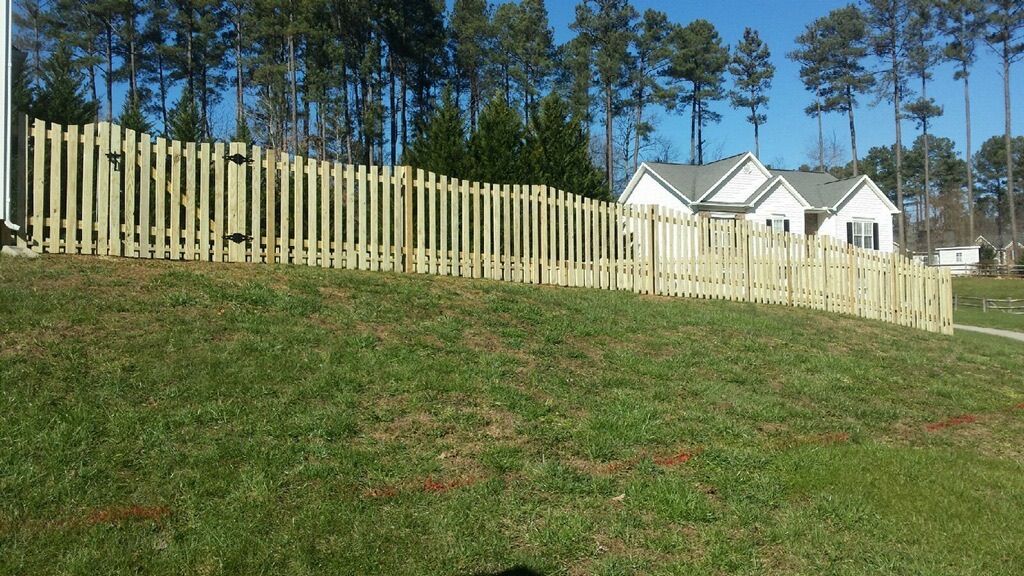 A wooden fence surrounds a lush green field in front of a house.