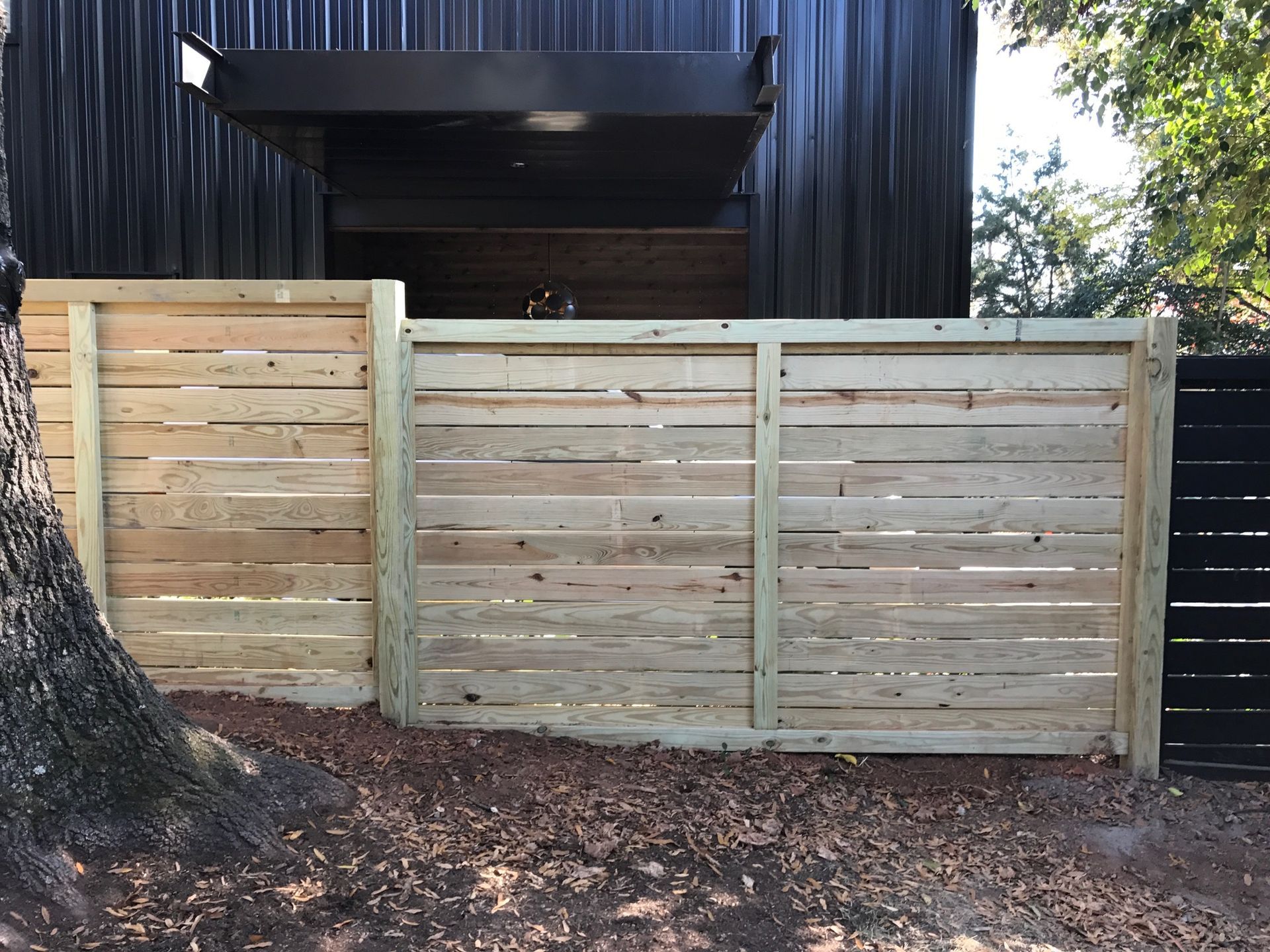 A wooden fence is surrounding a gravel driveway in front of a house.