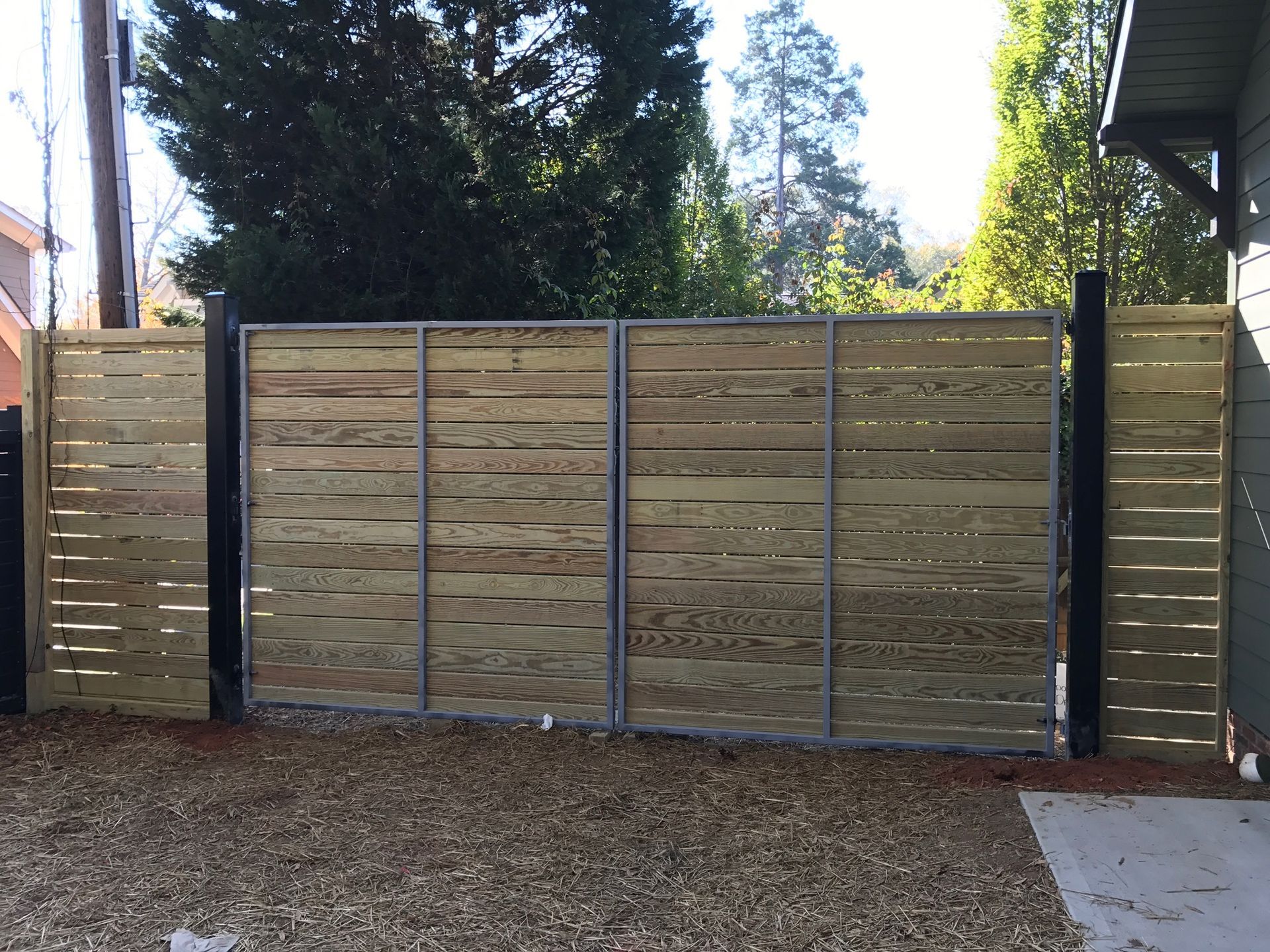 A wooden fence is surrounding a gravel driveway in front of a house.