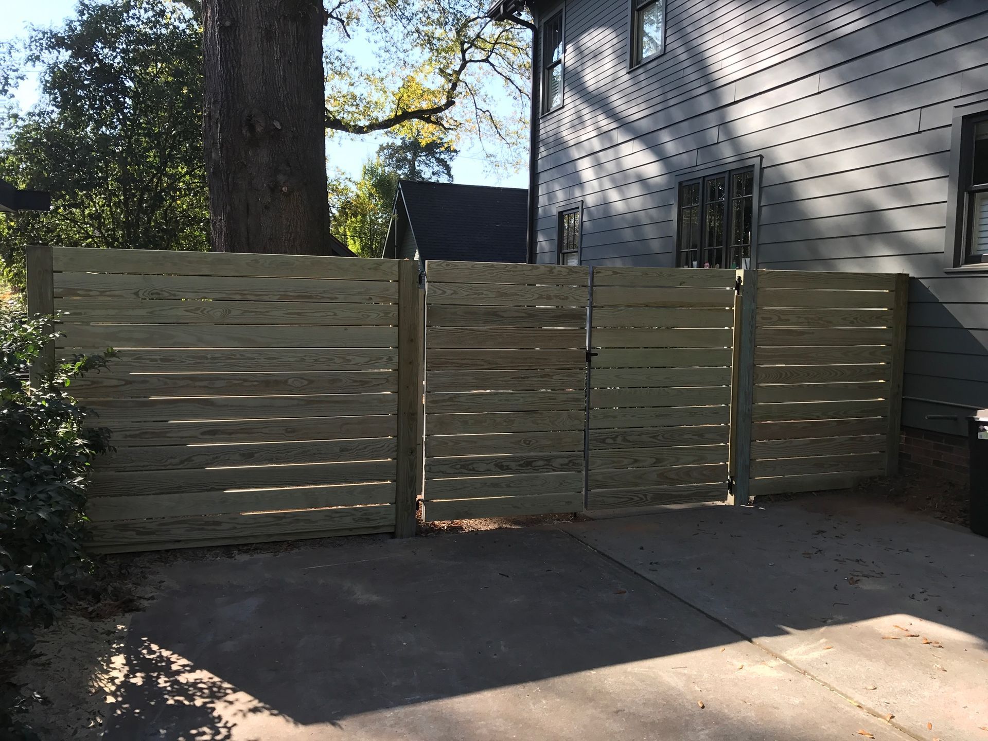 A wooden fence is surrounding a driveway in front of a house.