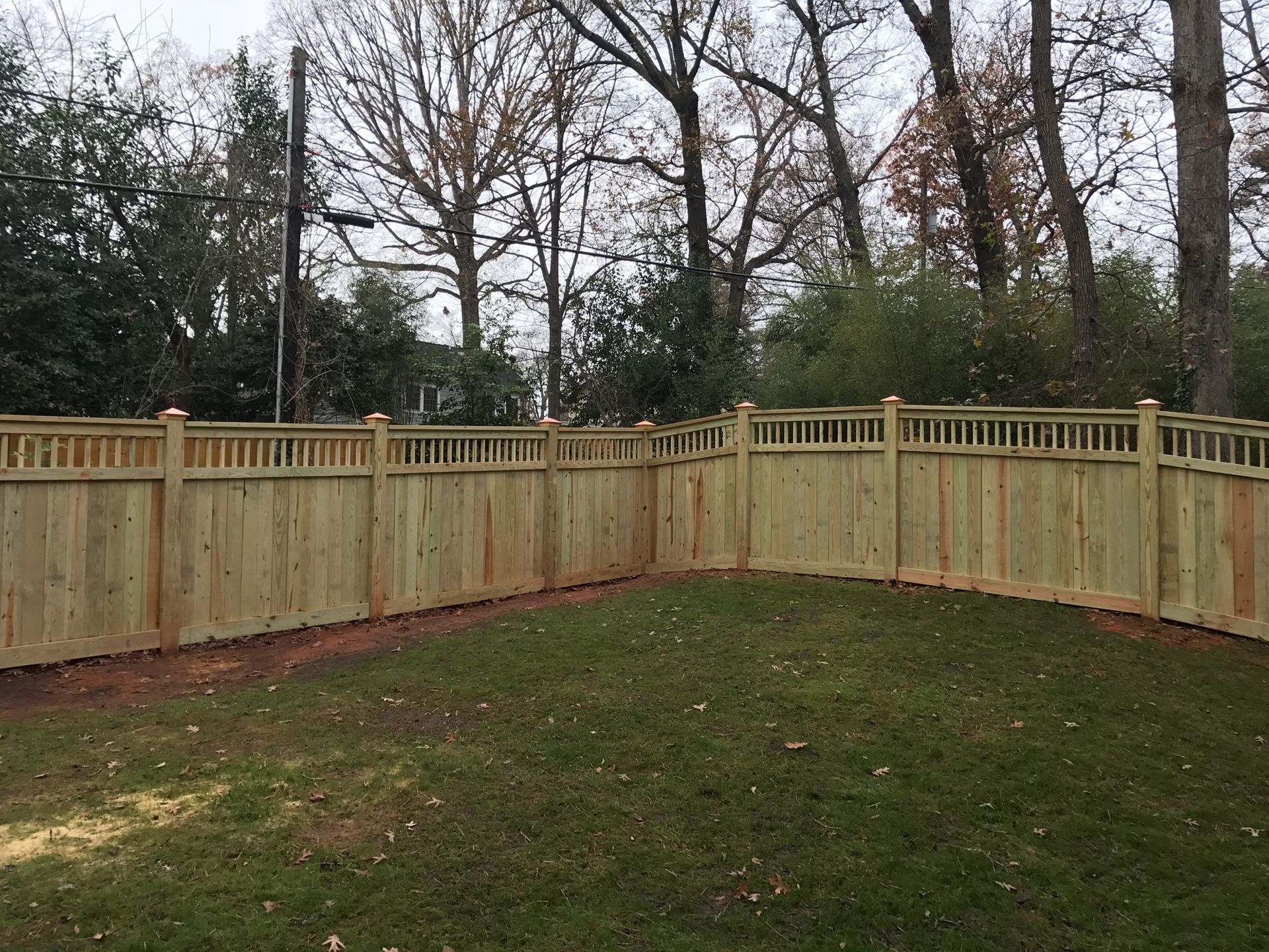 A wooden fence surrounds a lush green yard with trees in the background.